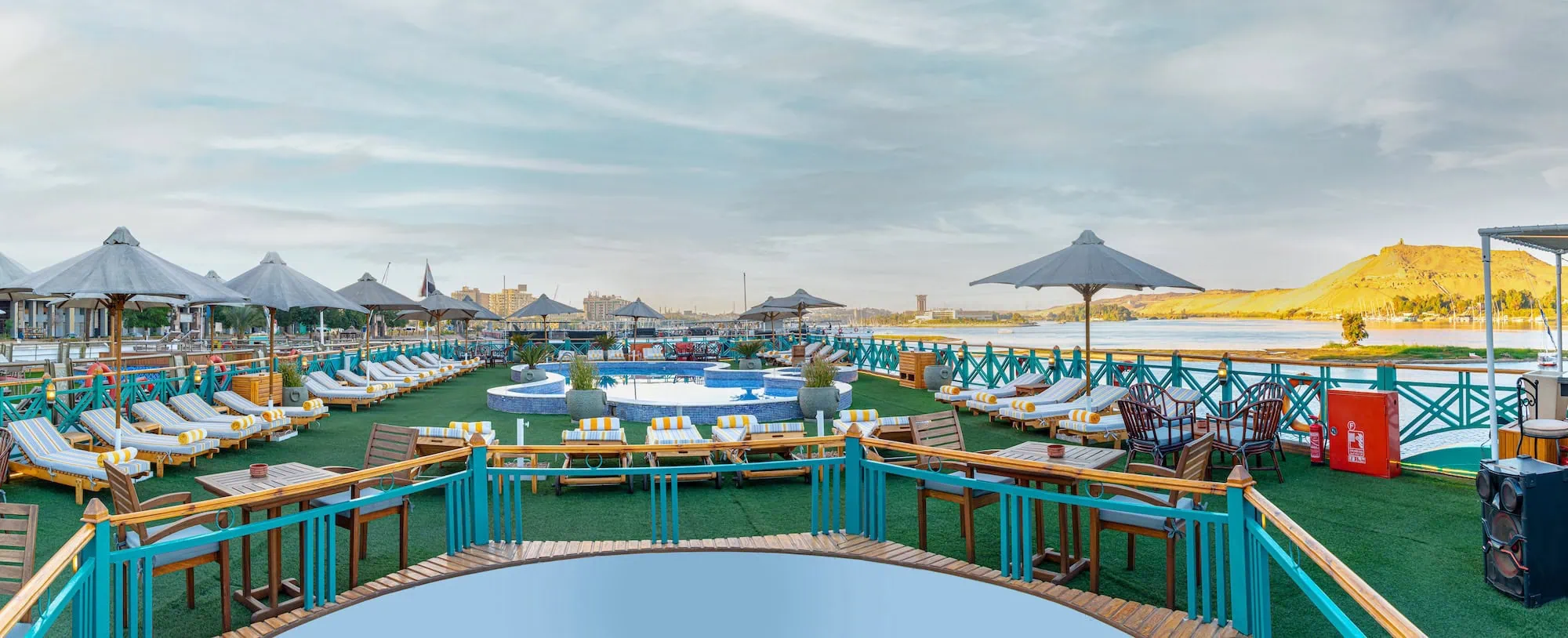Sun deck with swimming pool, loungers, and parasols on a 5-star Luxury Nile Cruise vessel sailing the Luxor–Aswan stretch of the Nile, the standard 4-day cruise included on most Egypt tours with Nile cruise.