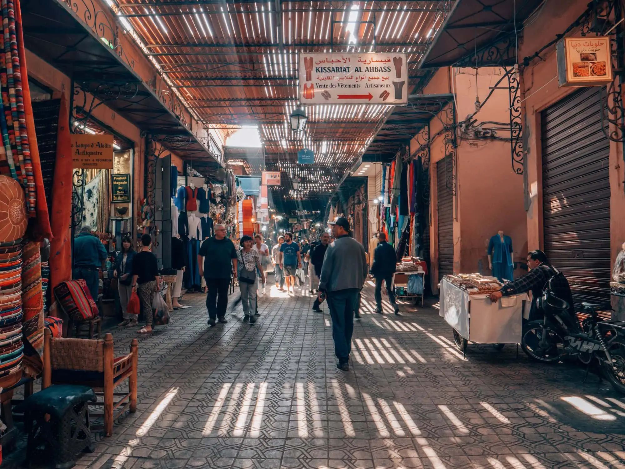 Interior view of traditional Moroccan souk marketplace with ornate metalwork canopy and bustling vendors