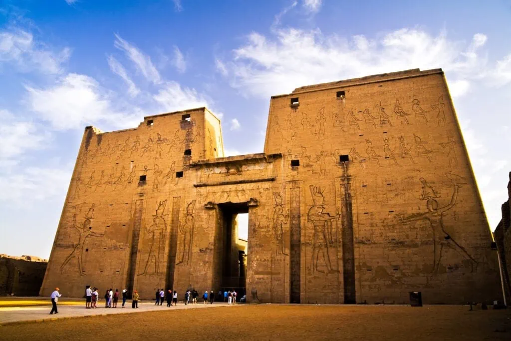 The 36-metre first pylon of the Temple of Horus at Edfu, with relief carvings and visitors at the base for scale, Egypt.