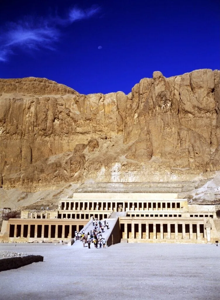 The three-terrace mortuary temple of Queen Hatshepsut at Deir el-Bahari on Luxor's West Bank, set against the natural cliff face below the Theban peak (al-Qurn), dedicated to the 18th Dynasty pharaoh Hatshepsut who reigned 1479–1458 BC, a standard shore excursion on the West Bank day of the Luxor–Aswan cruise.