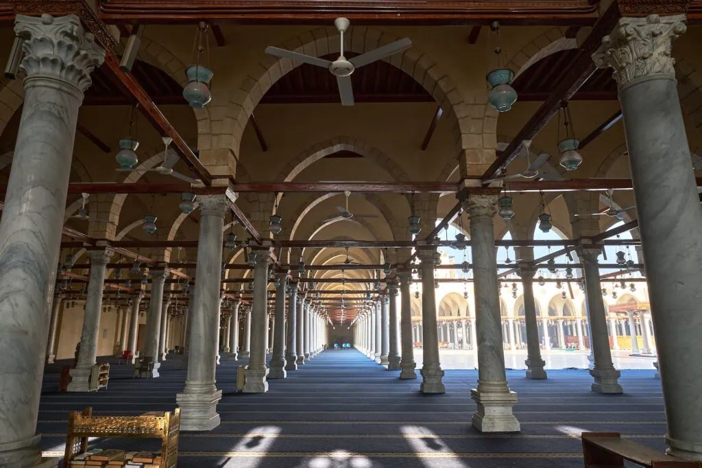 Rows of marble columns, stone arches, hanging lamps, and prayer carpets inside the Mosque of Amr ibn al-As, Old Cairo, Cairo
