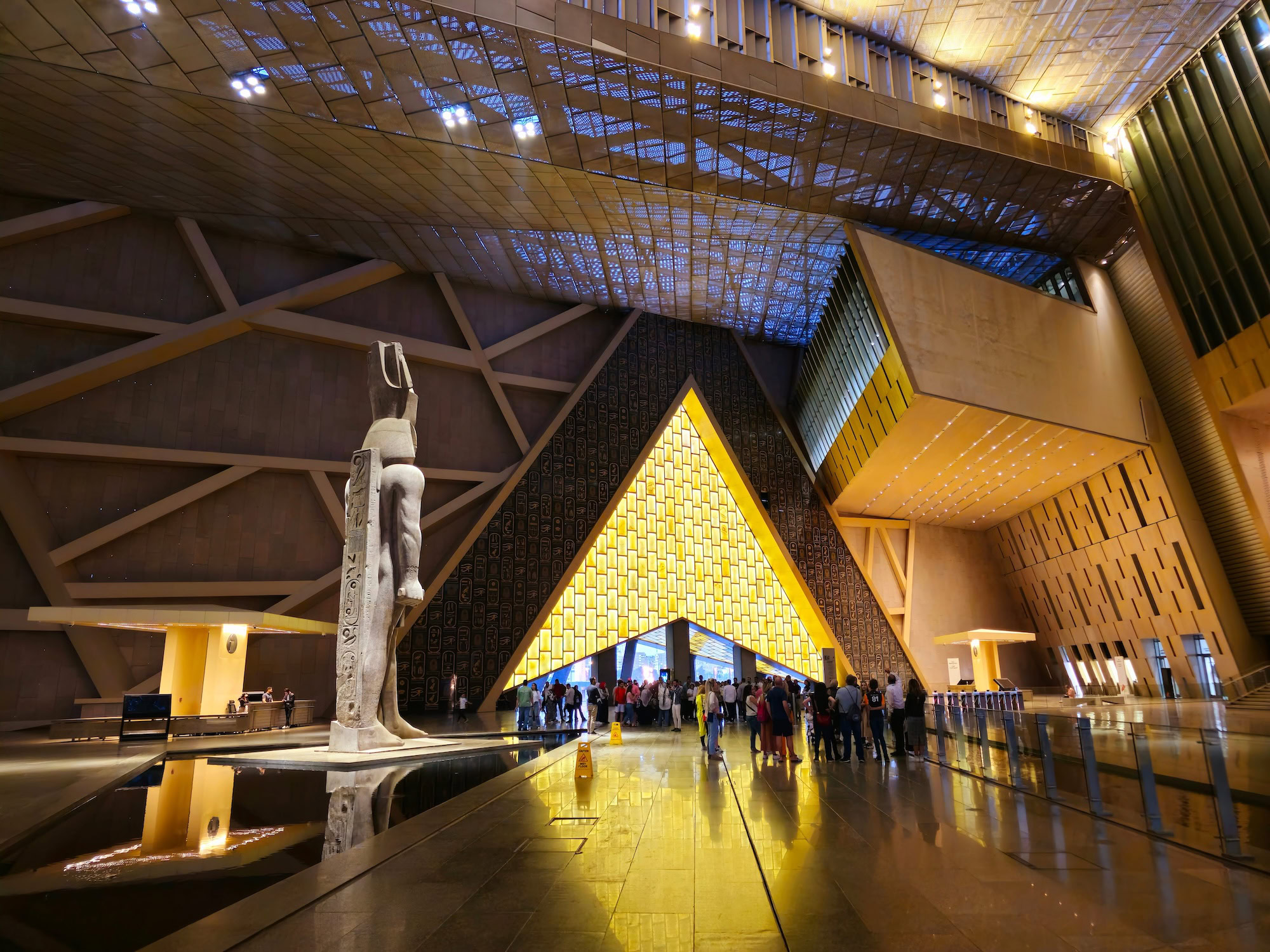 Interior of Grand Egyptian Museum showing pyramid structure with golden geometric ceiling and Egyptian statue