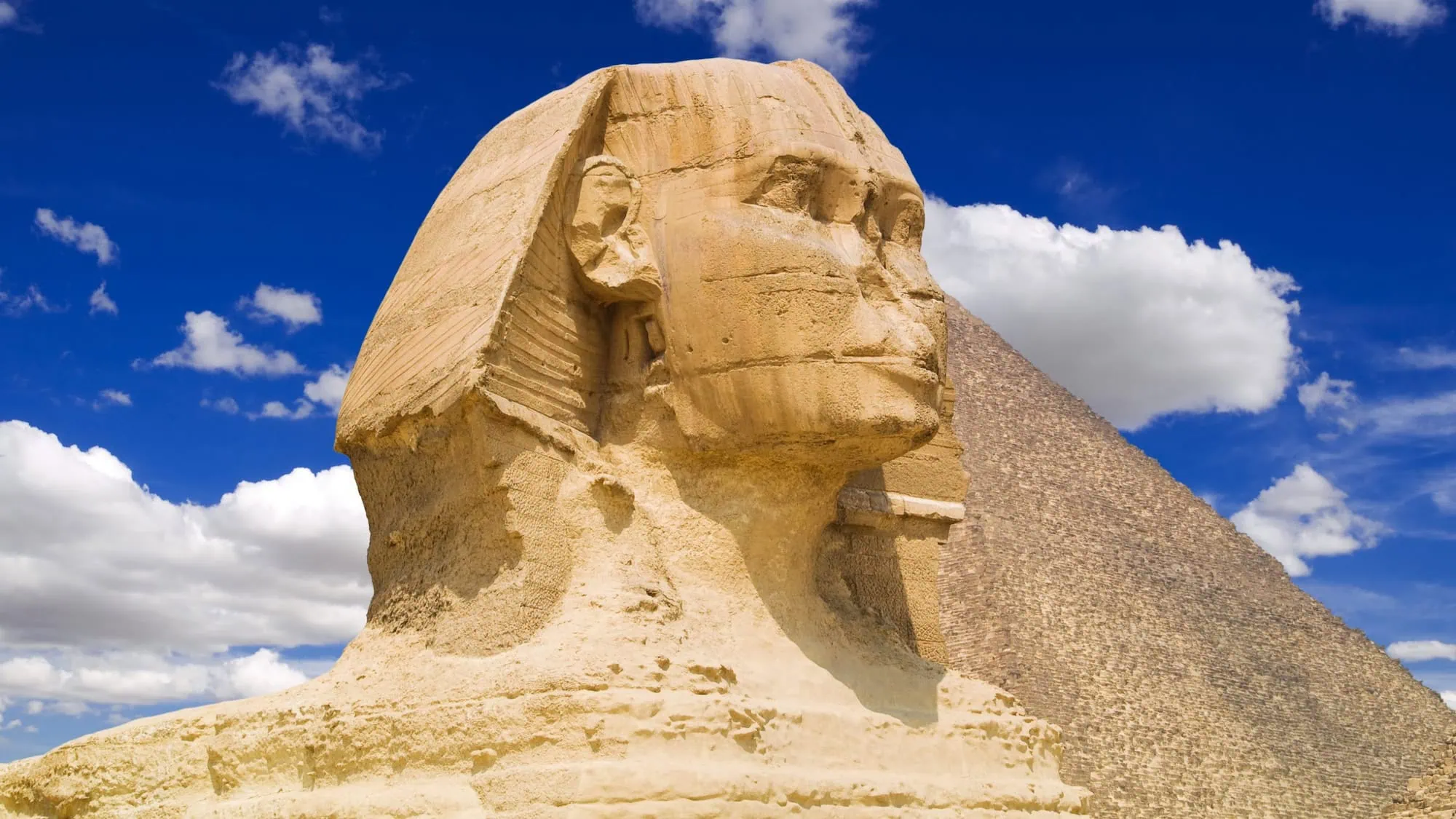 Great Sphinx of Giza with pyramid in background under cloudy sky