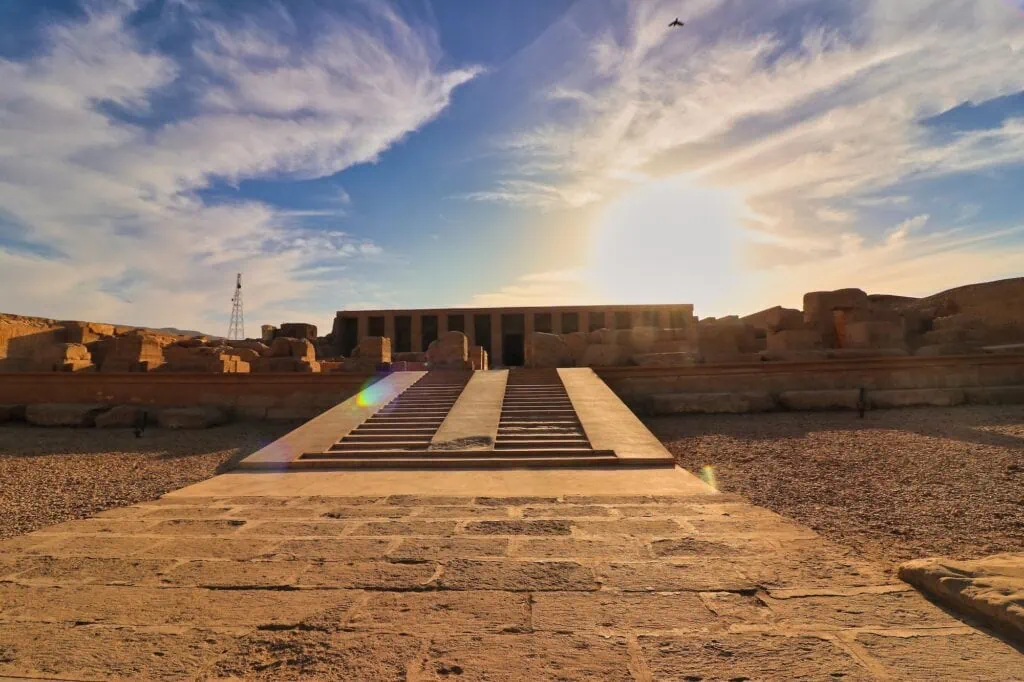 The facade and entrance steps of the Great Temple of Seti I at Abydos in the afternoon sun, a 13th-century BC temple north of Luxor with its pillared front and stone forecourt visible.
