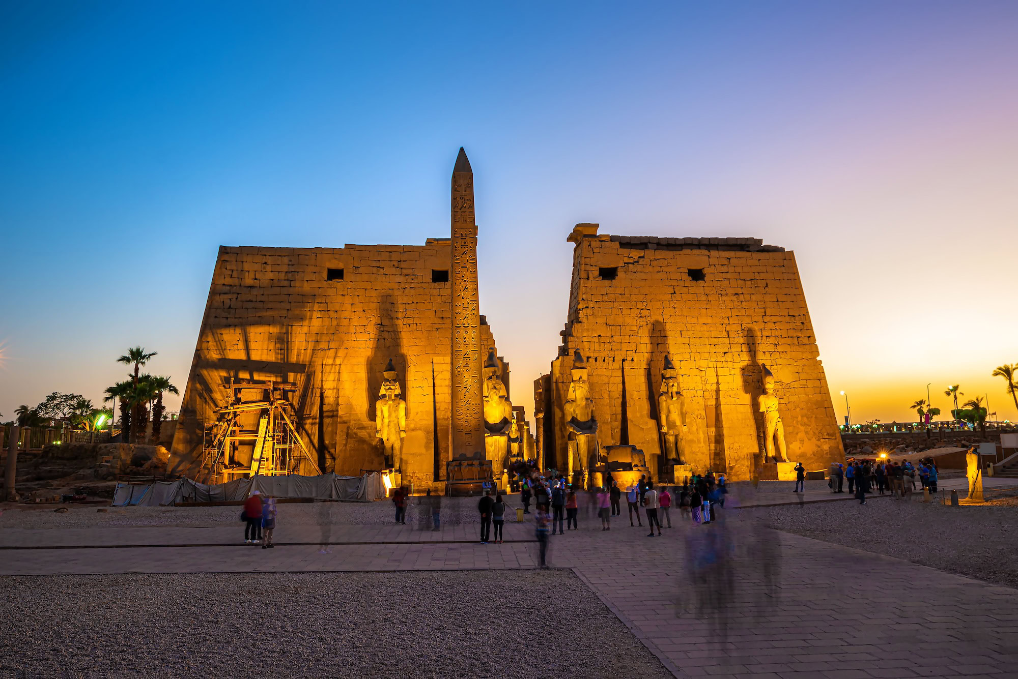 Ancient Luxor Temple complex featuring towering obelisk, pharaoh statues, and massive stone columns