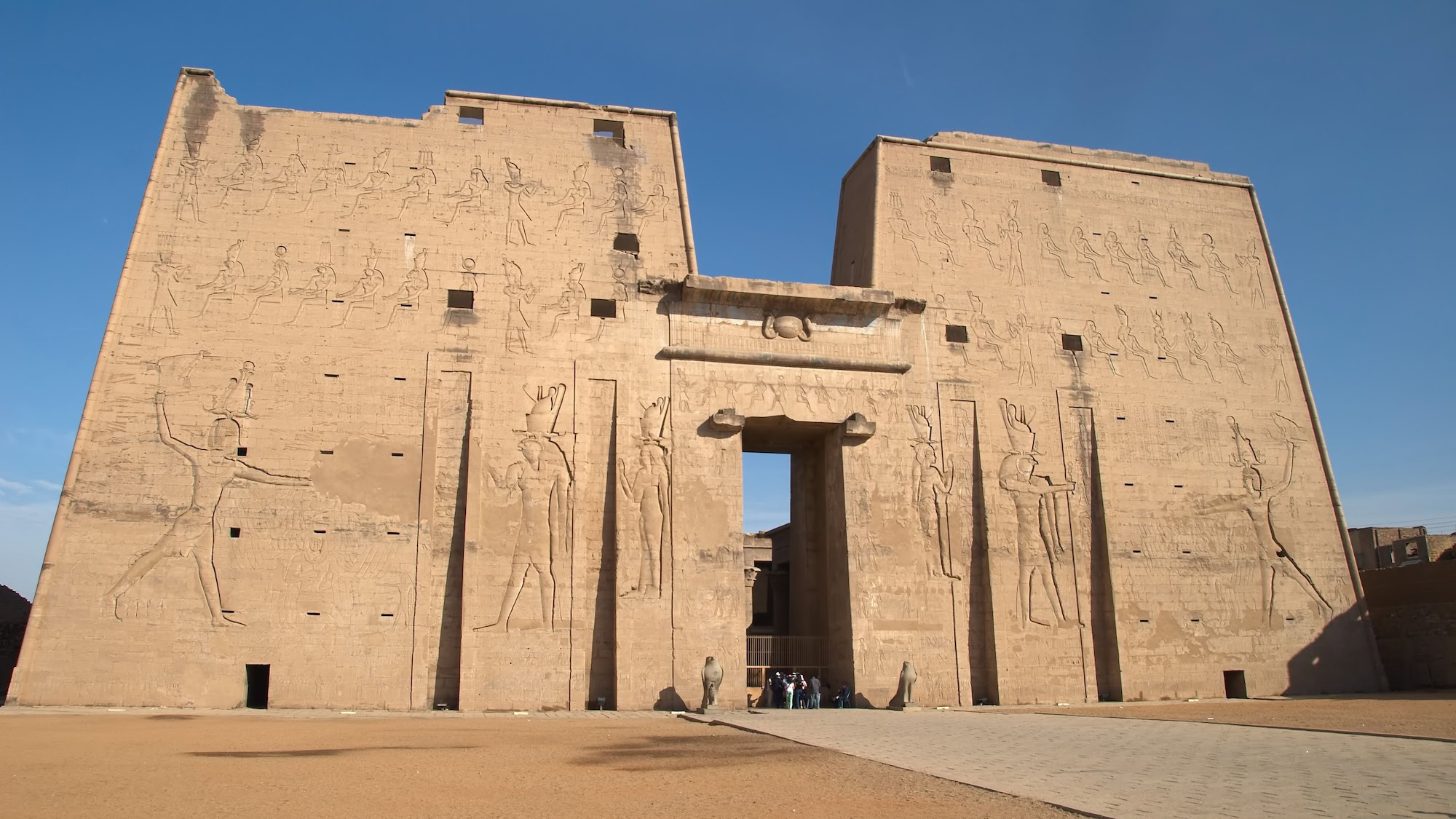 Ancient Edfu Temple entrance with massive stone pylon towers and carved hieroglyphic reliefs