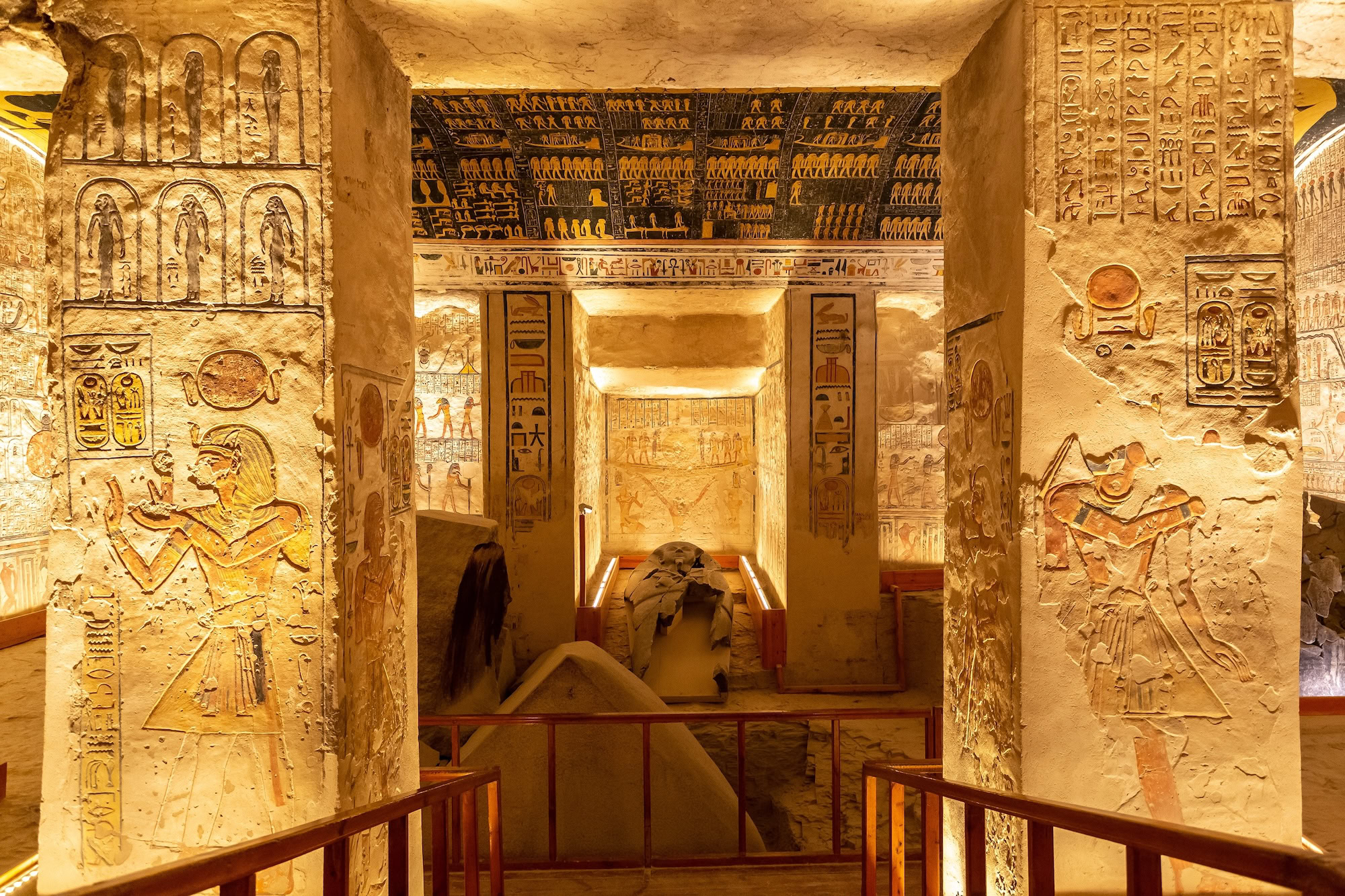 Ancient Egyptian burial chamber with hieroglyphic wall carvings and wooden railings