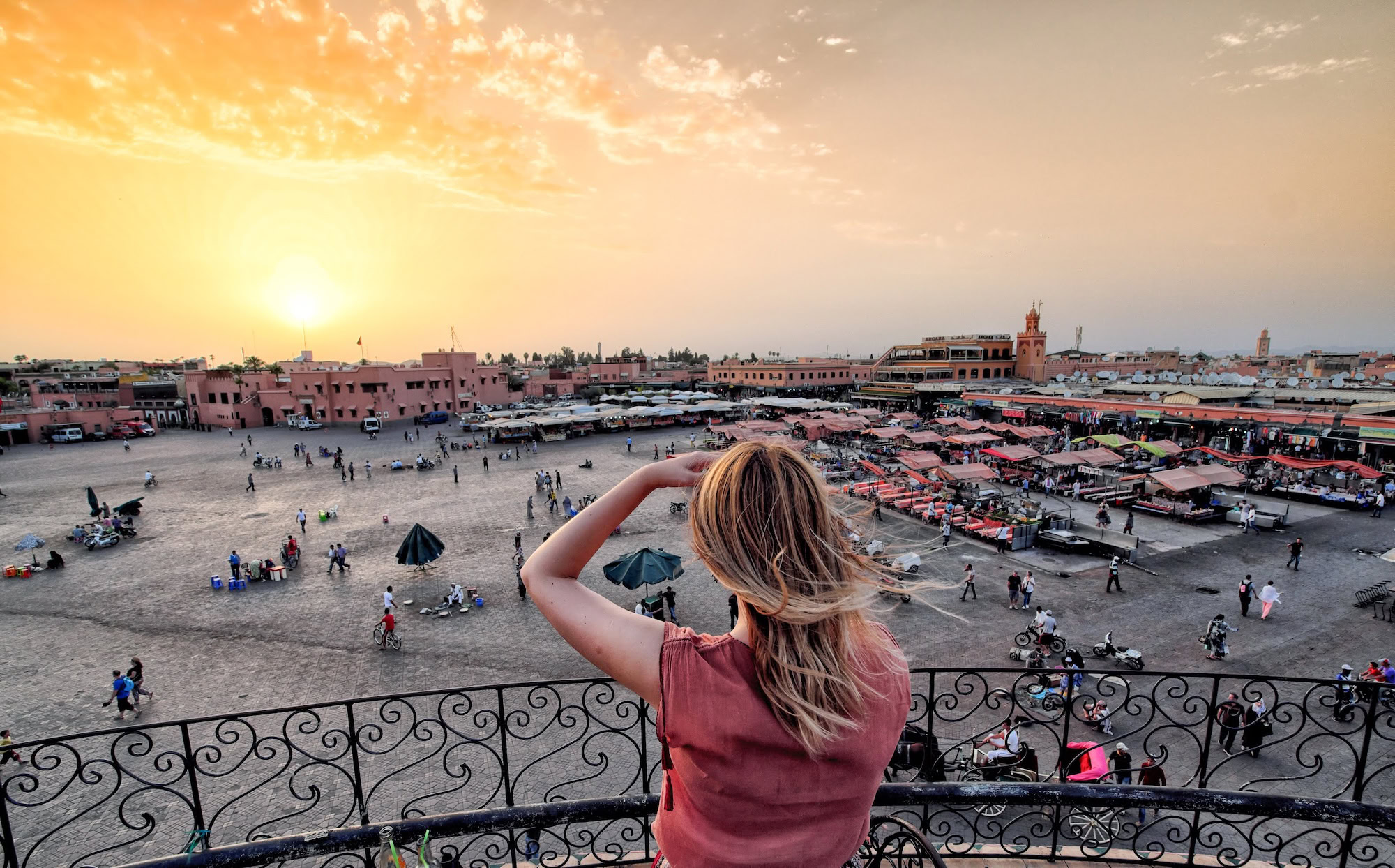 Woman on balcony overlooking vibrant Jemaa el-Fnaa square with market stalls and traditional Marrakech architecture