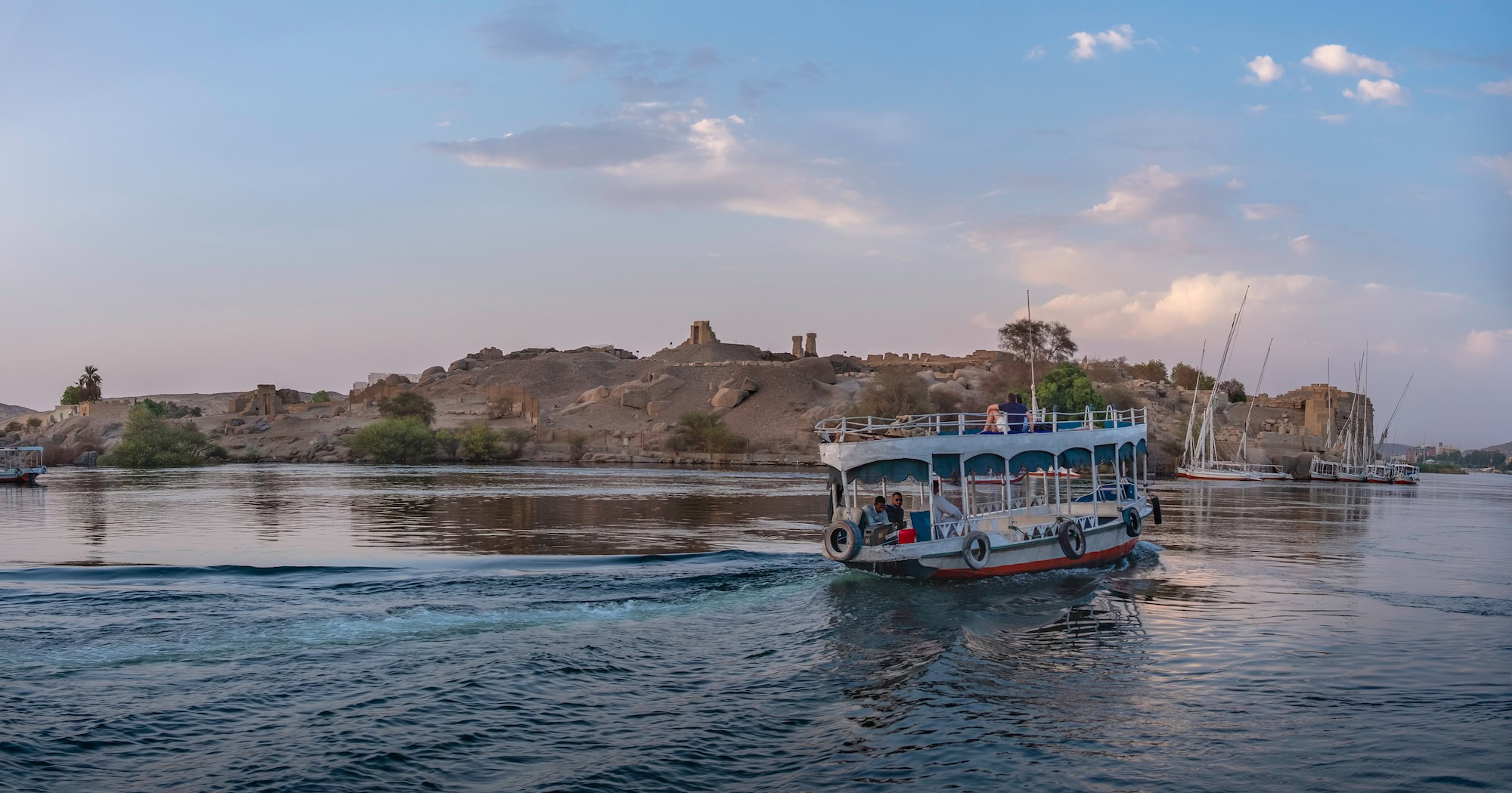 Boat approaching Elephantine Island with ancient ruins and palm trees along the Nile River in Aswan
