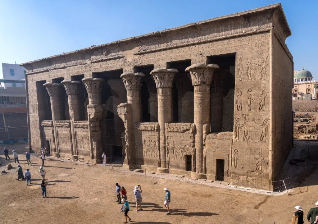 Visitors standing before the well-preserved stone facade and carved reliefs of the Temple of Esna, Esna