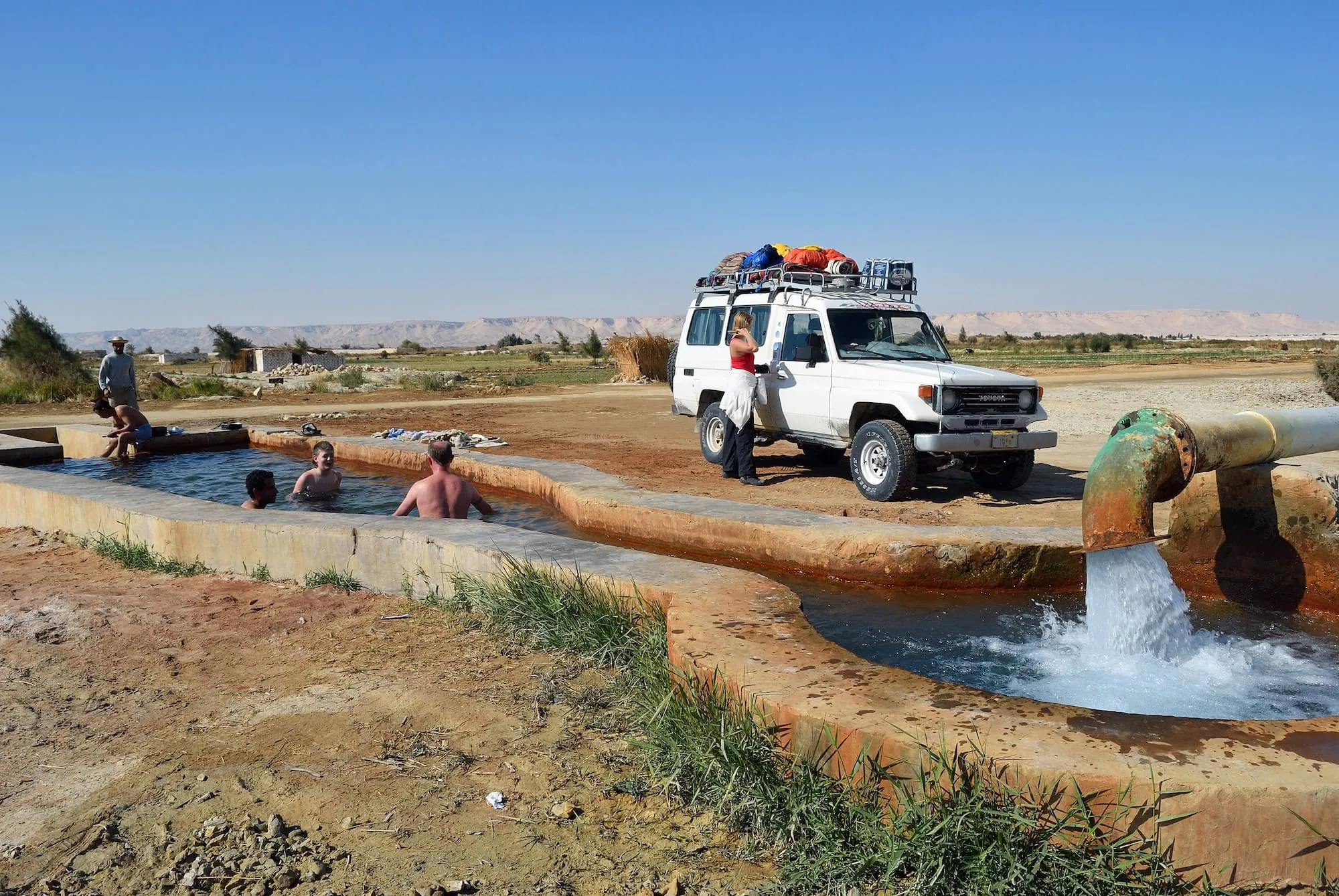 Remote natural hot springs in desert with vehicle and camping equipment