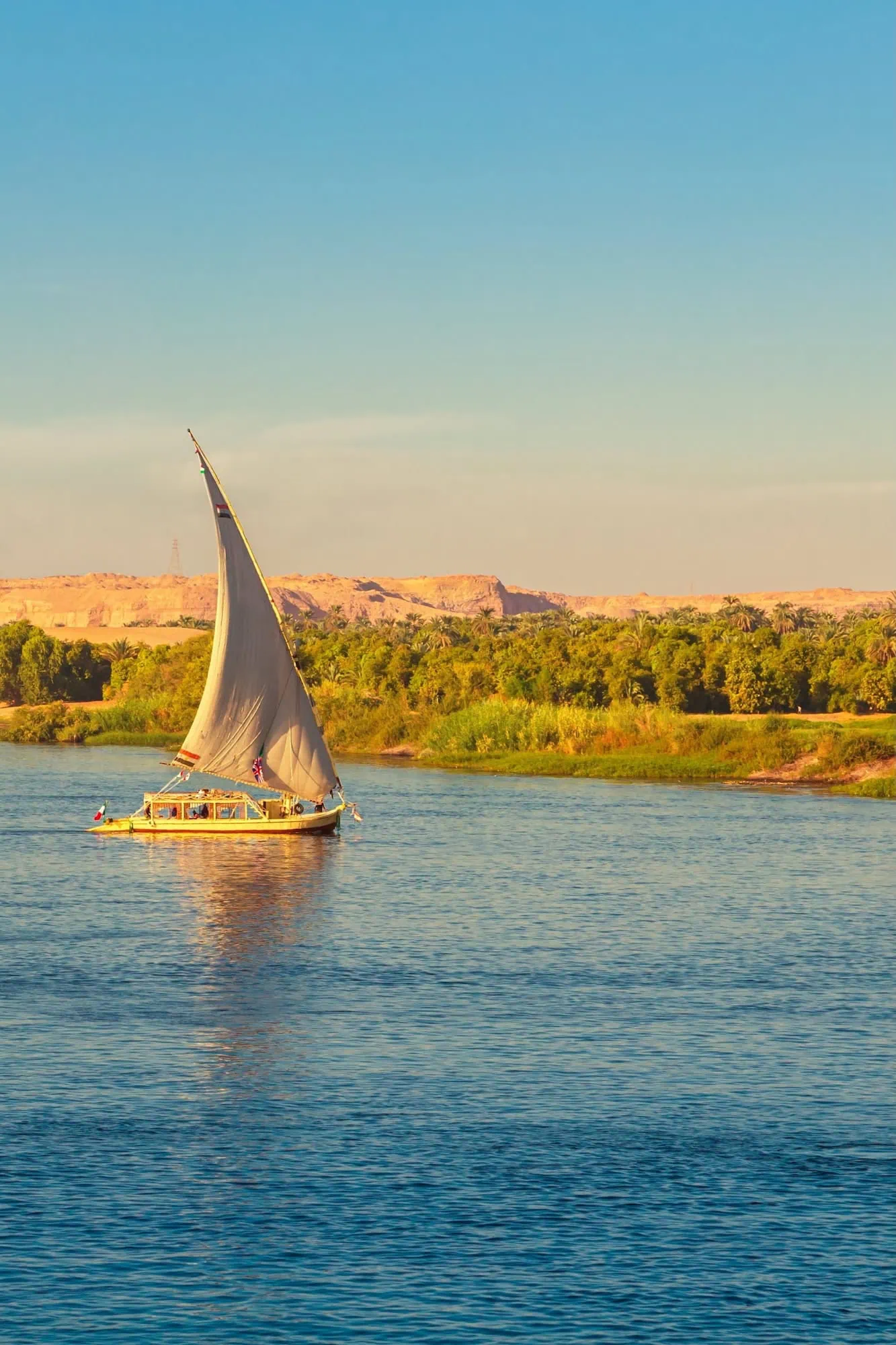 Traditional Egyptian felucca with single triangular lateen sail catching sunset light on the Nile near Aswan, southern Egypt