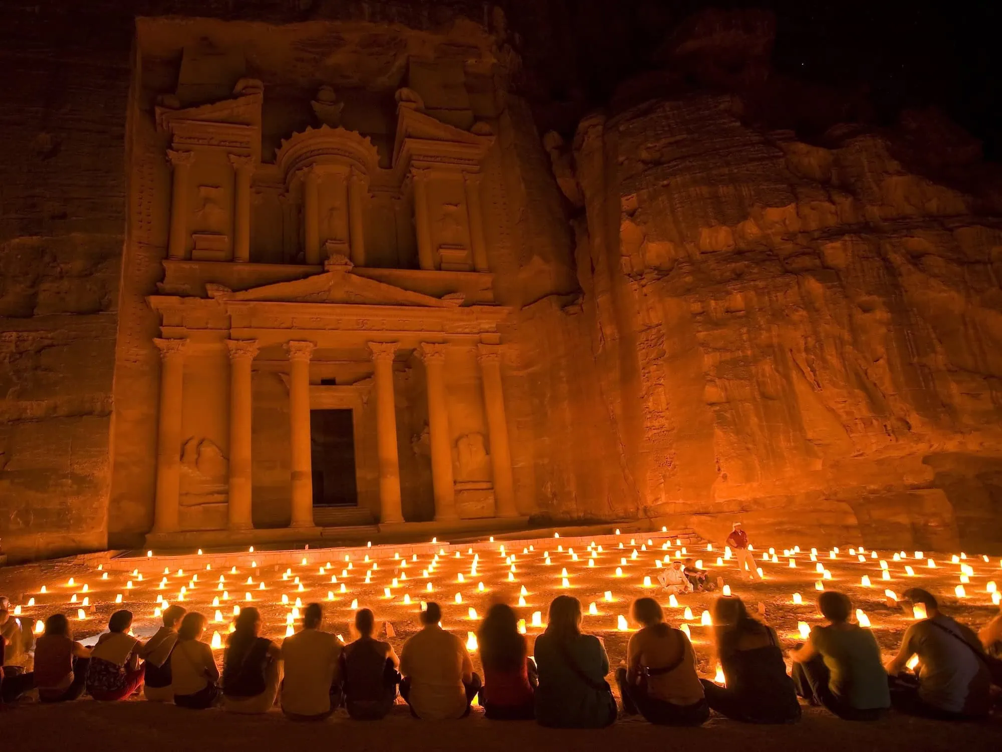 Treasury in Petra illuminated by candlelight with visitors seated in front