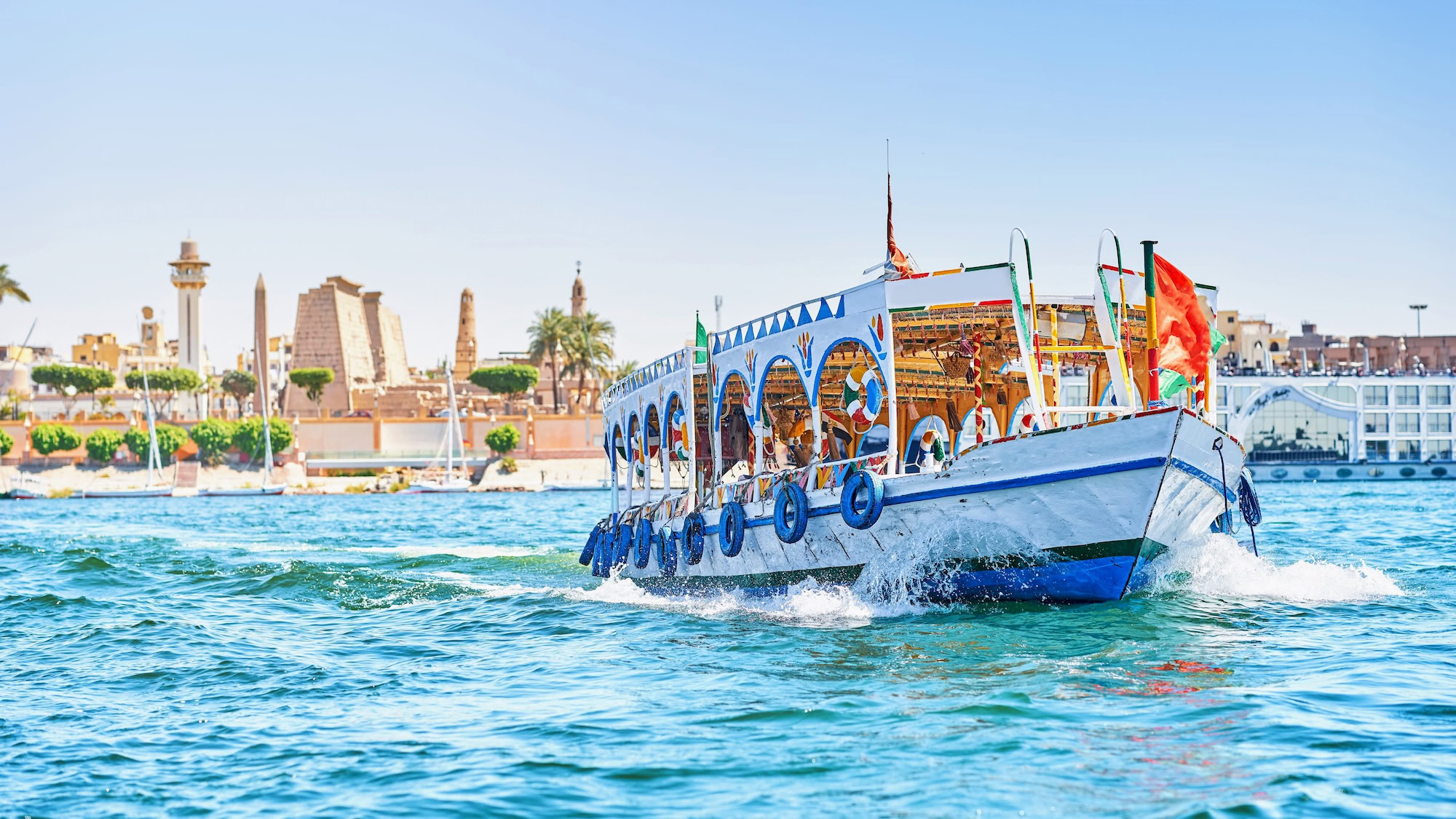 Traditional boat on Nile River with ancient Luxor Temple and palm trees in background