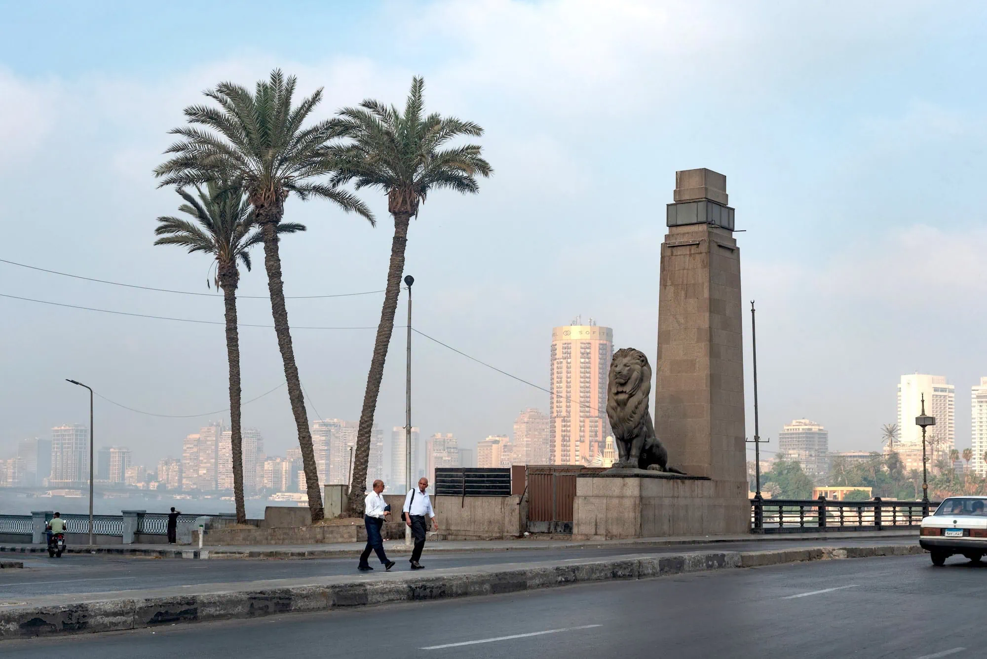 Street scene in Cairo with lion statue, people walking, and urban cityscape