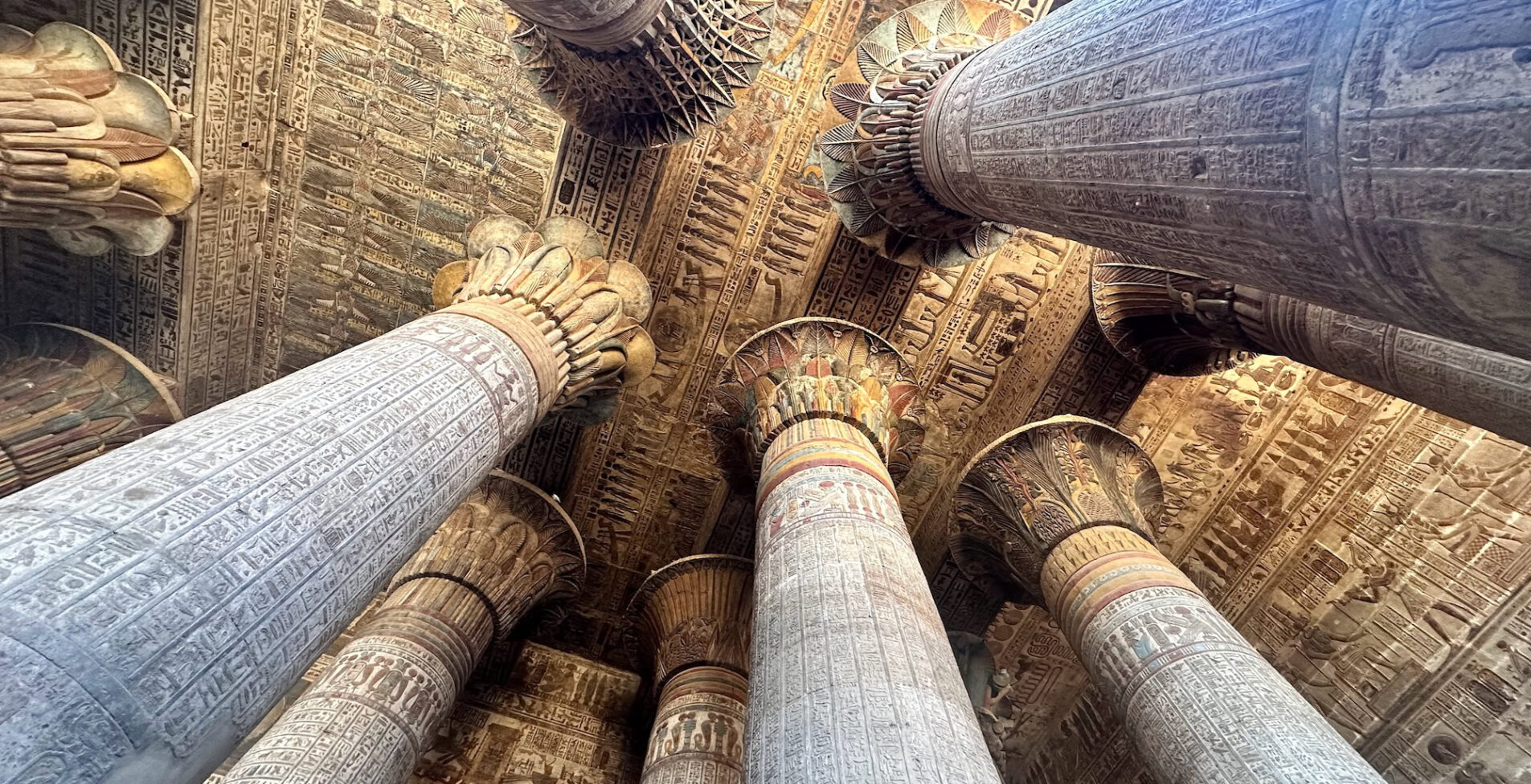 Upward view of painted stone columns and hieroglyph covered ceiling inside the Temple of Khnum Esna