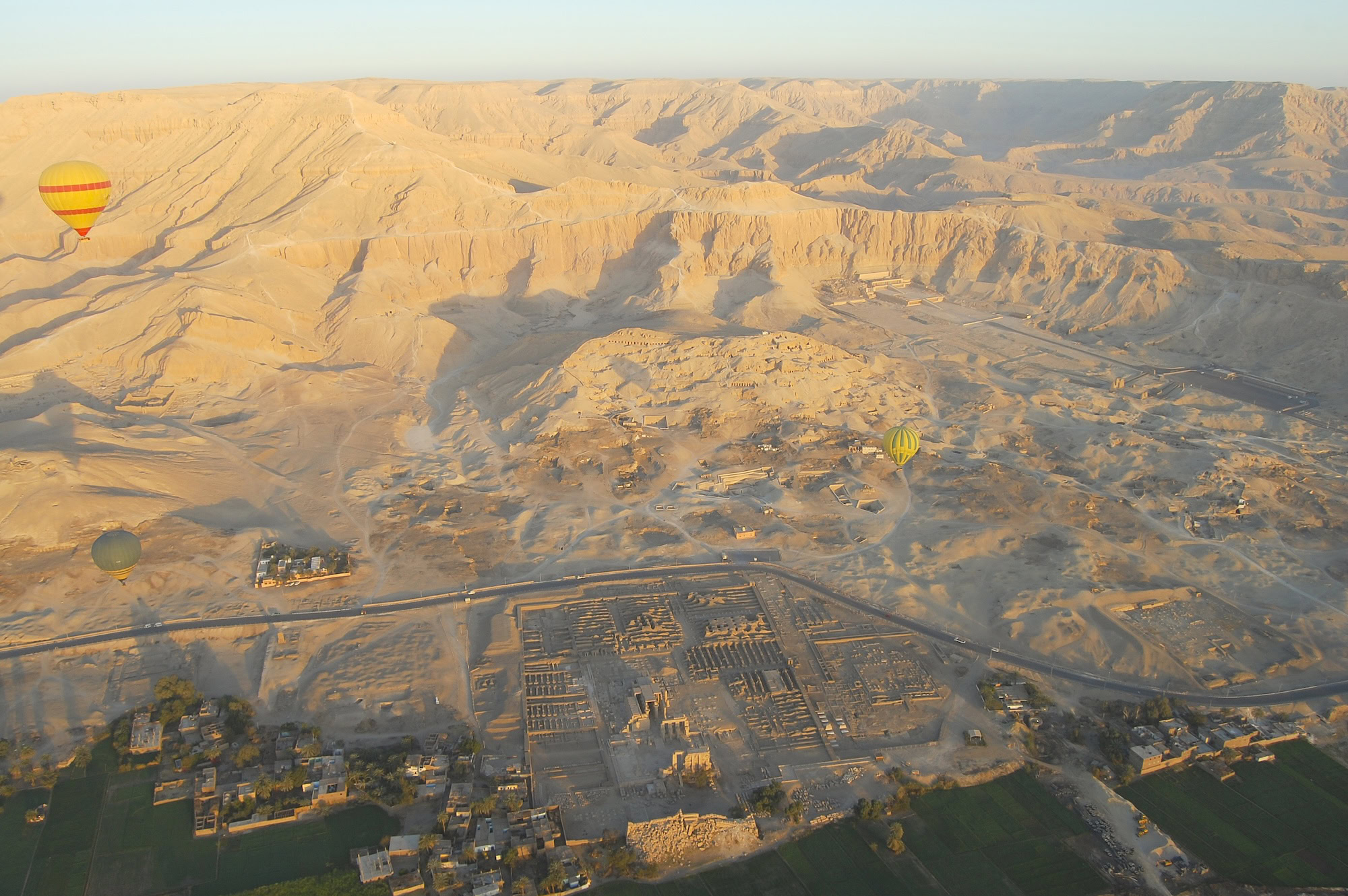 Aerial view of Valley of the Kings showing ancient temple complex and desert mountains with hot air balloons