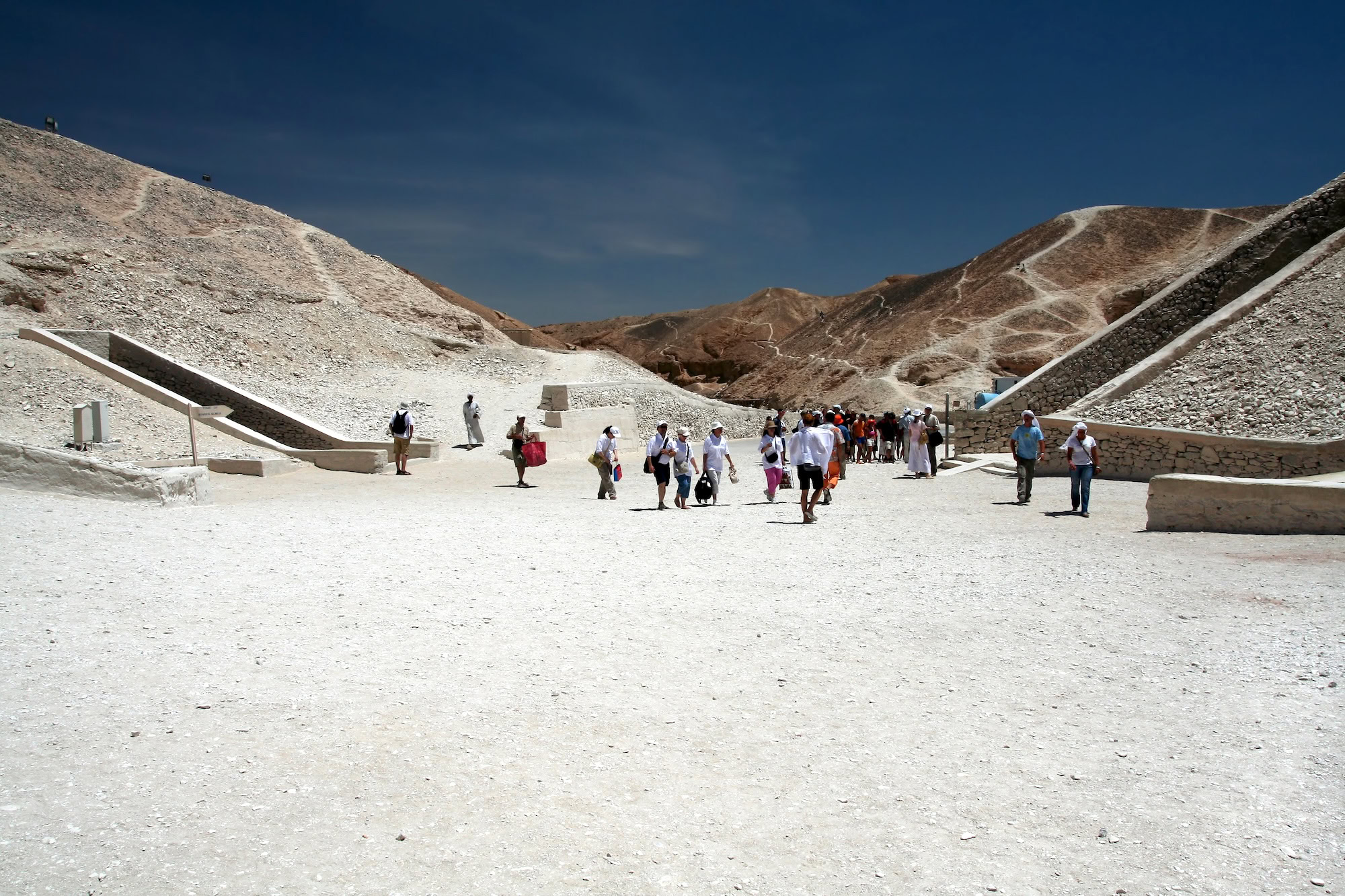 Tourists walking along pathways at Valley of the Kings entrance with desert hills