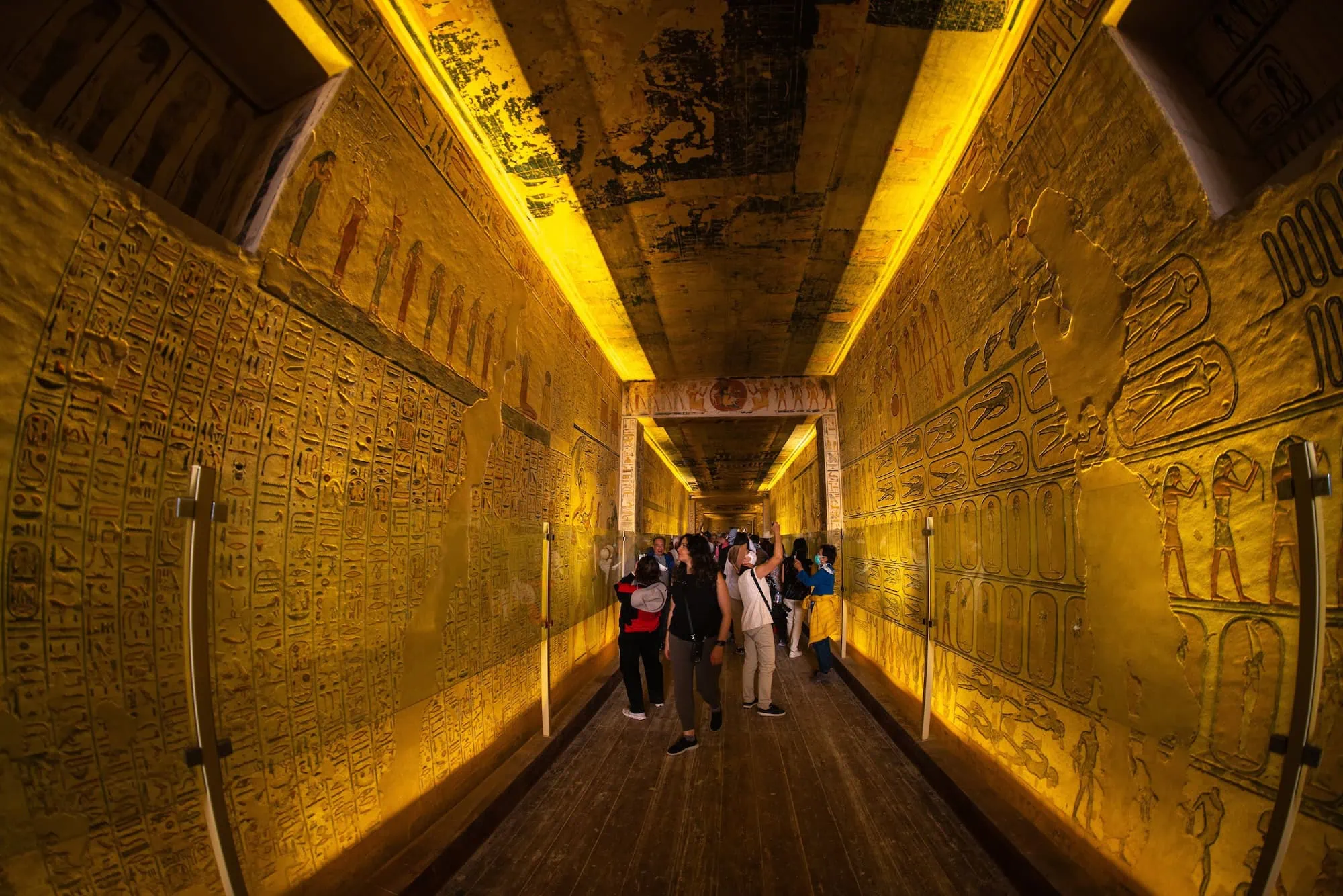 Interior of ancient Egyptian tomb showing illuminated hieroglyphic wall paintings and stone corridors