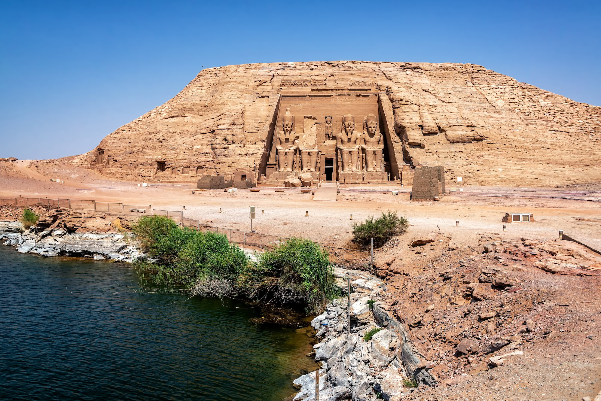 Abu Simbel temples beside Lake Nasser with cliff face and vegetation