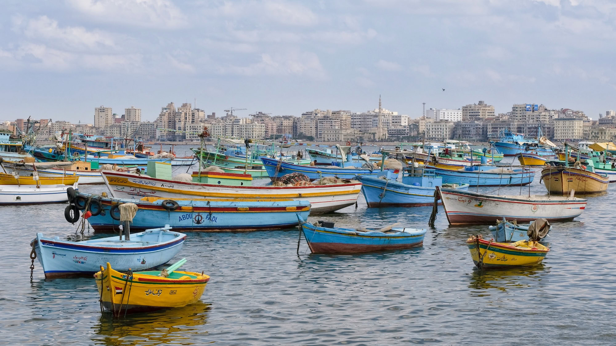 Fishing boats in Alexandria harbor with cityscape and cloudy sky
