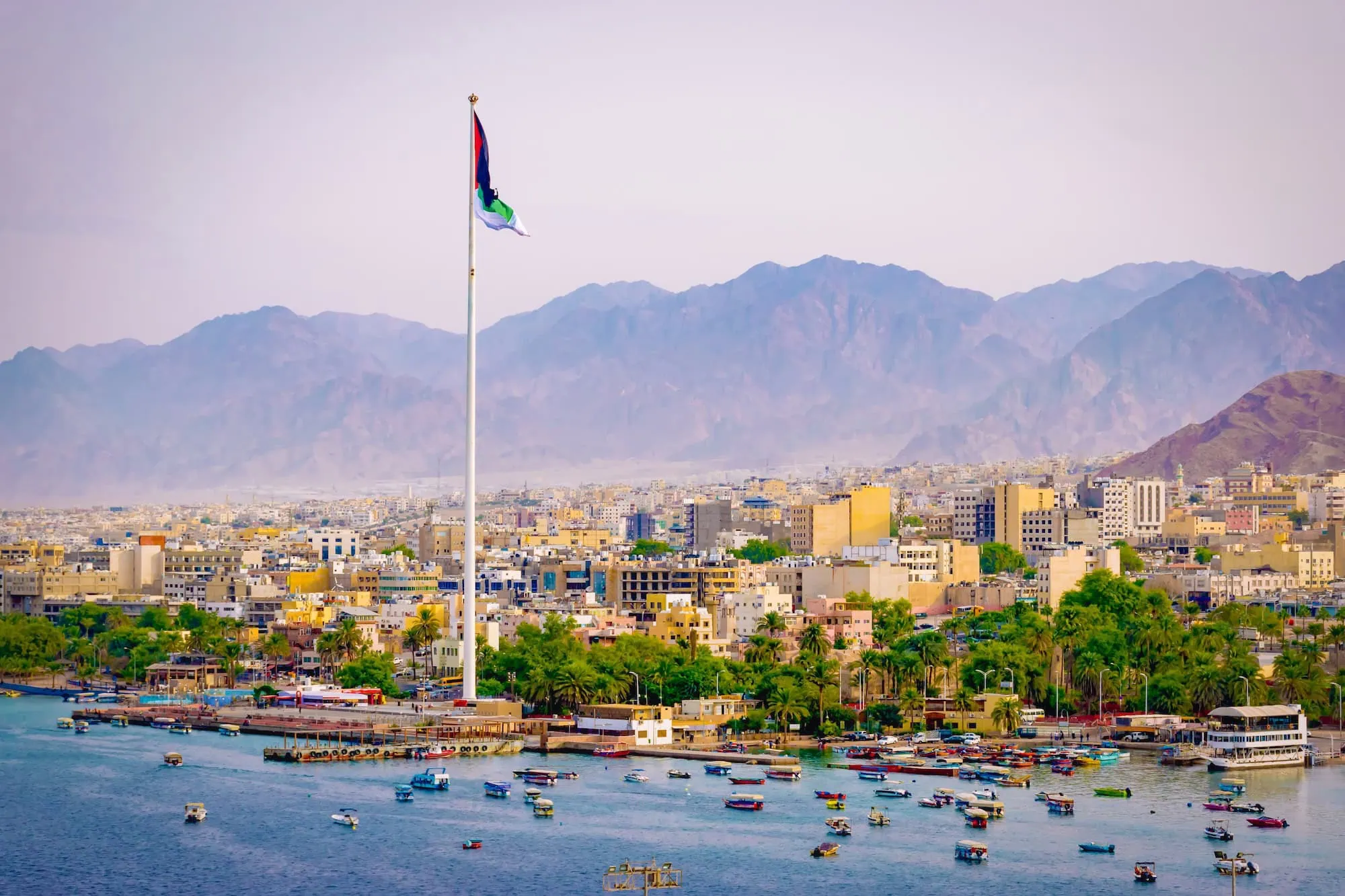 Aqaba port waterfront with flag, mountains, and harbor boats
