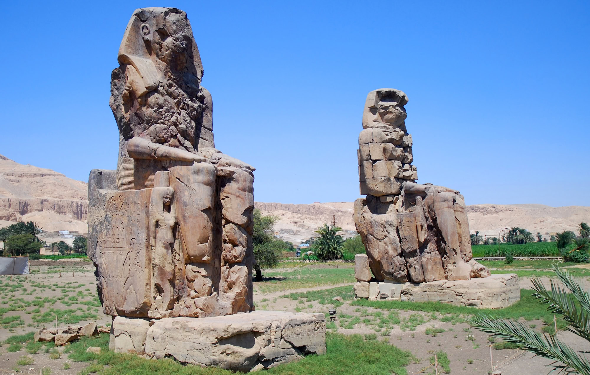 Ancient Colossi of Memnon statues with hieroglyphic inscriptions in Luxor desert landscape
