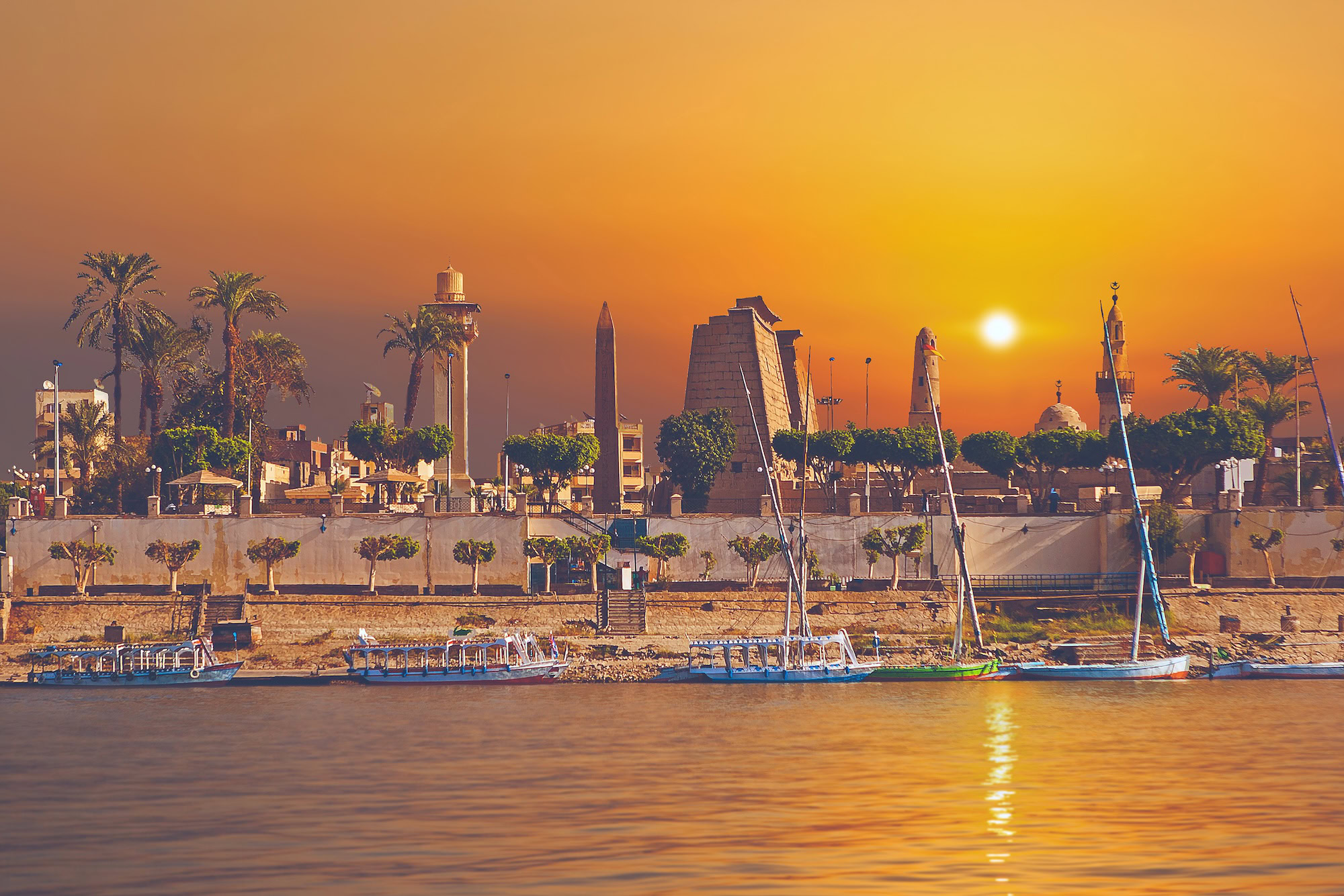 Vista panoramica del maestoso Tempio di Luxor al tramonto con obelisco, feluca tradizionale sul Nilo e palme