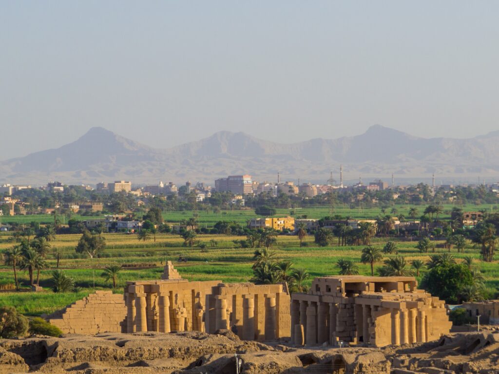 View of the Ramesseum temple ruins set against green cultivated fields and distant desert mountains, Luxor
