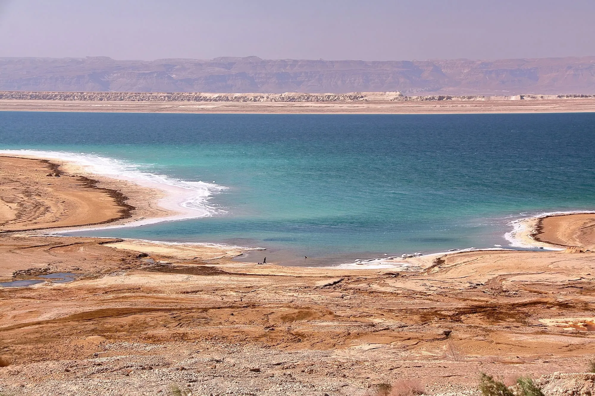 Panoramic view of Dead Sea with turquoise water, white salt formations and desert mountains