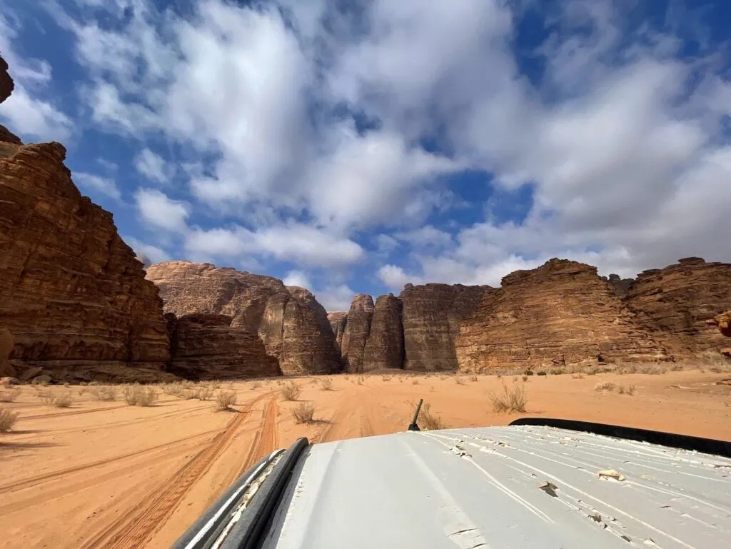 Four-wheel-drive vehicle traveling across open desert sand with rock formations in Wadi Rum, Wadi Rum