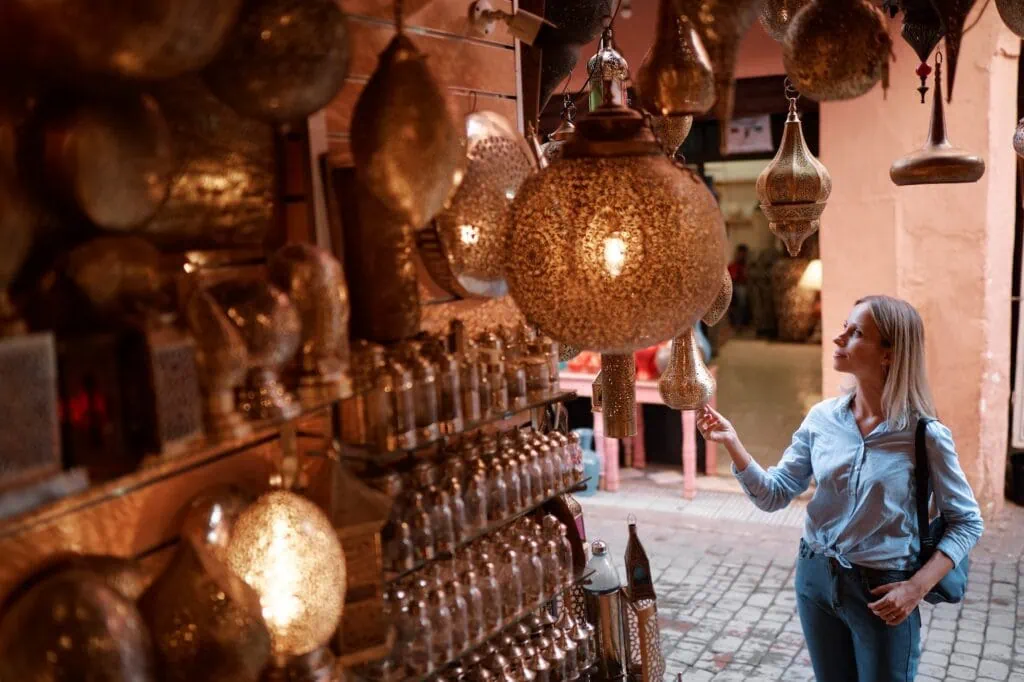 Marrakesh souk stall displaying hanging metal lanterns and shelves of decorative items with a visitor browsing Marrakech