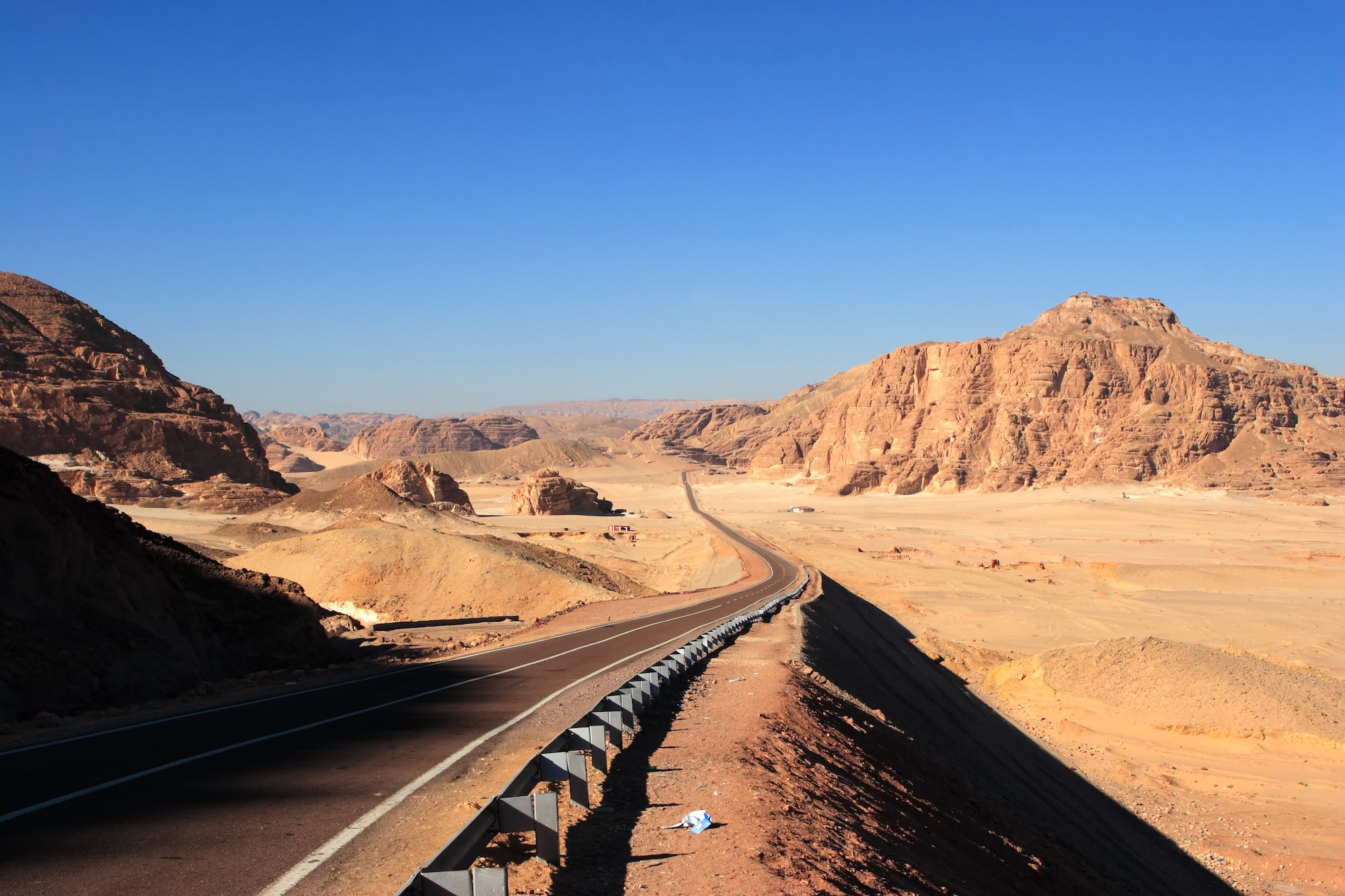 Desert highway cutting through rocky cliffs and mountainous terrain