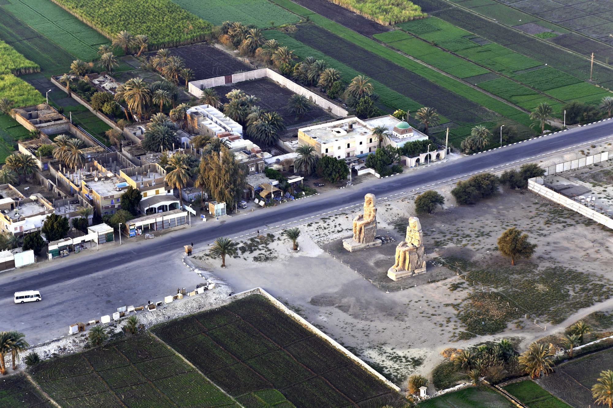 Aerial view of the massive Colossi of Memnon statues rising from the Egyptian desert landscape