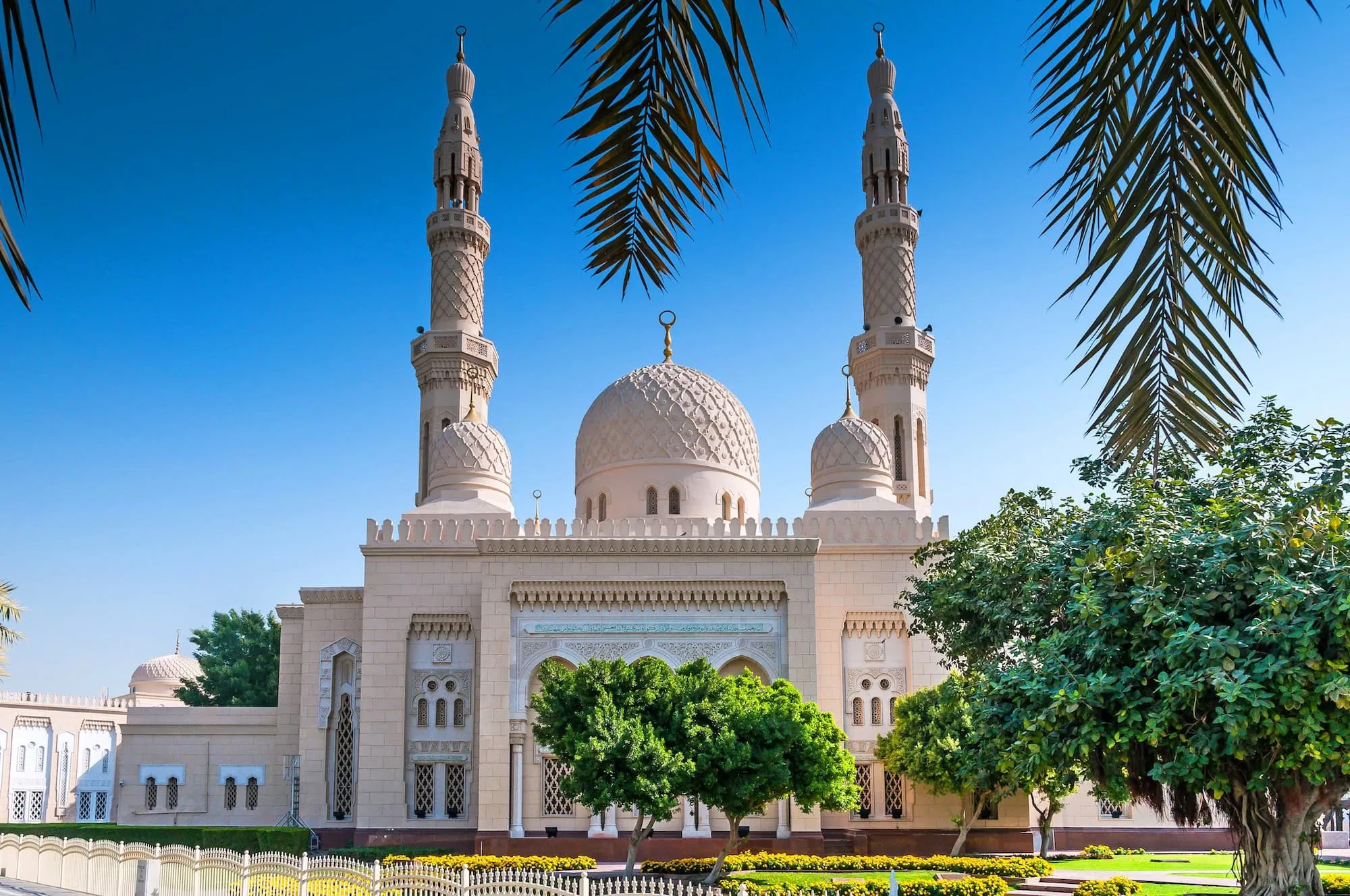 White stone Jumeirah Mosque with twin minarets and central dome surrounded by palm trees