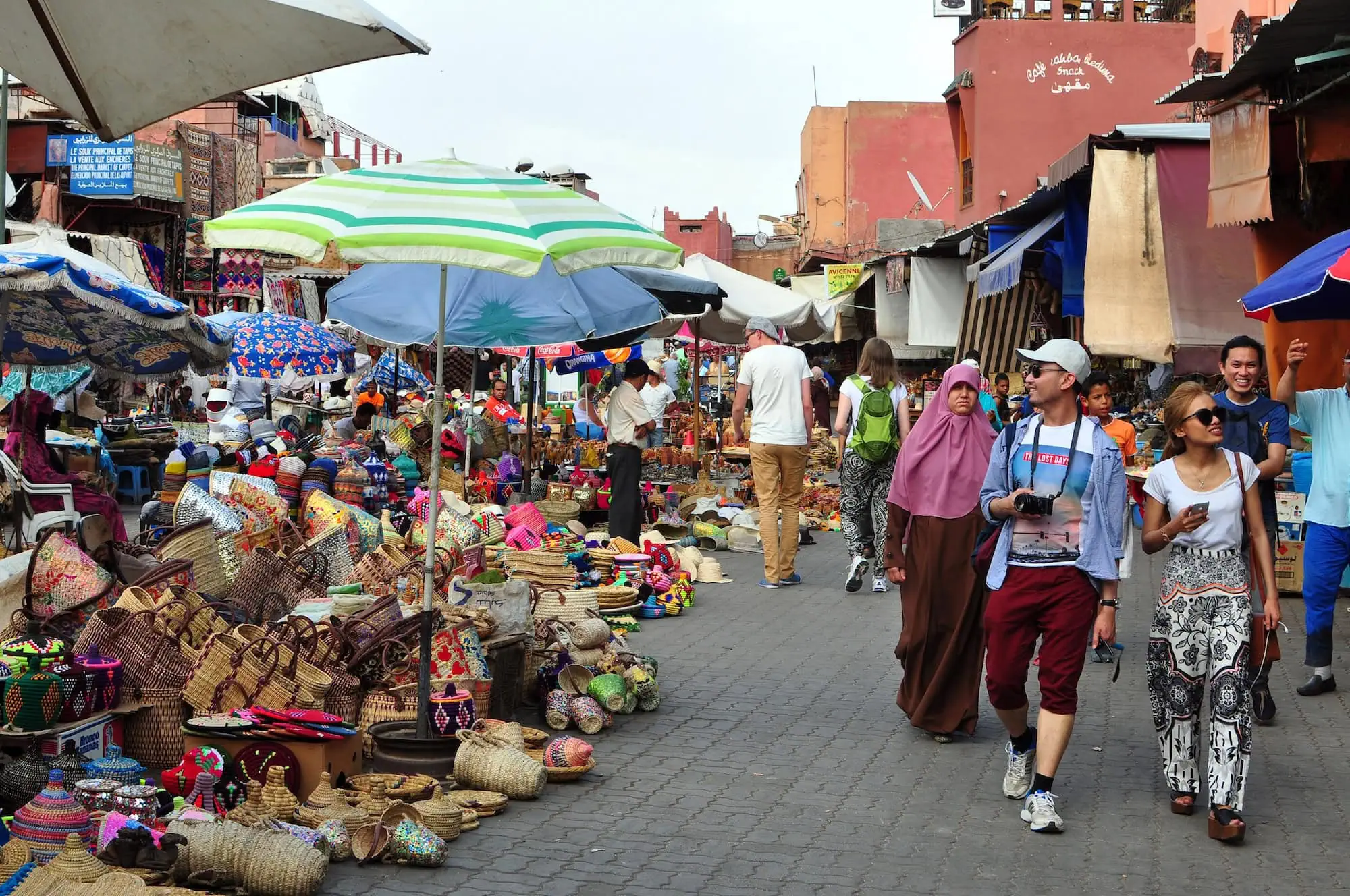 Bustling market street in Marrakech's medina with colorful stalls and traditional pink buildings