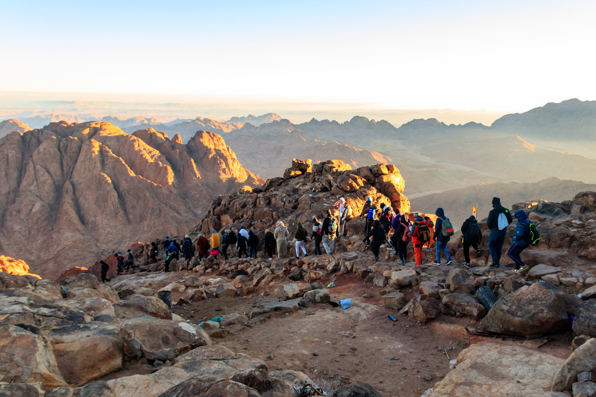 Hikers with backpacks climbing rocky mountain terrain at Mount Sinai during sunrise