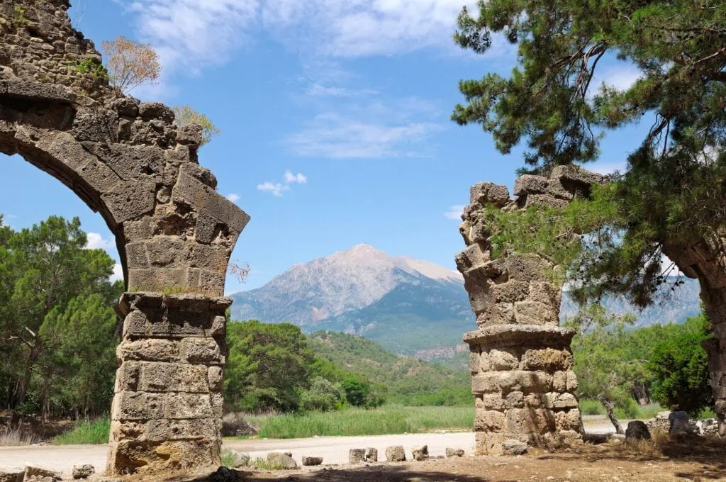 Ruins of Phaselis with stone remains among coastal trees and Mount Olympos in the background