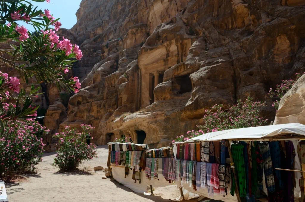 Textile shop with colorful fabrics displayed in front of a carved rock facade at Little Petra Wadi Musa