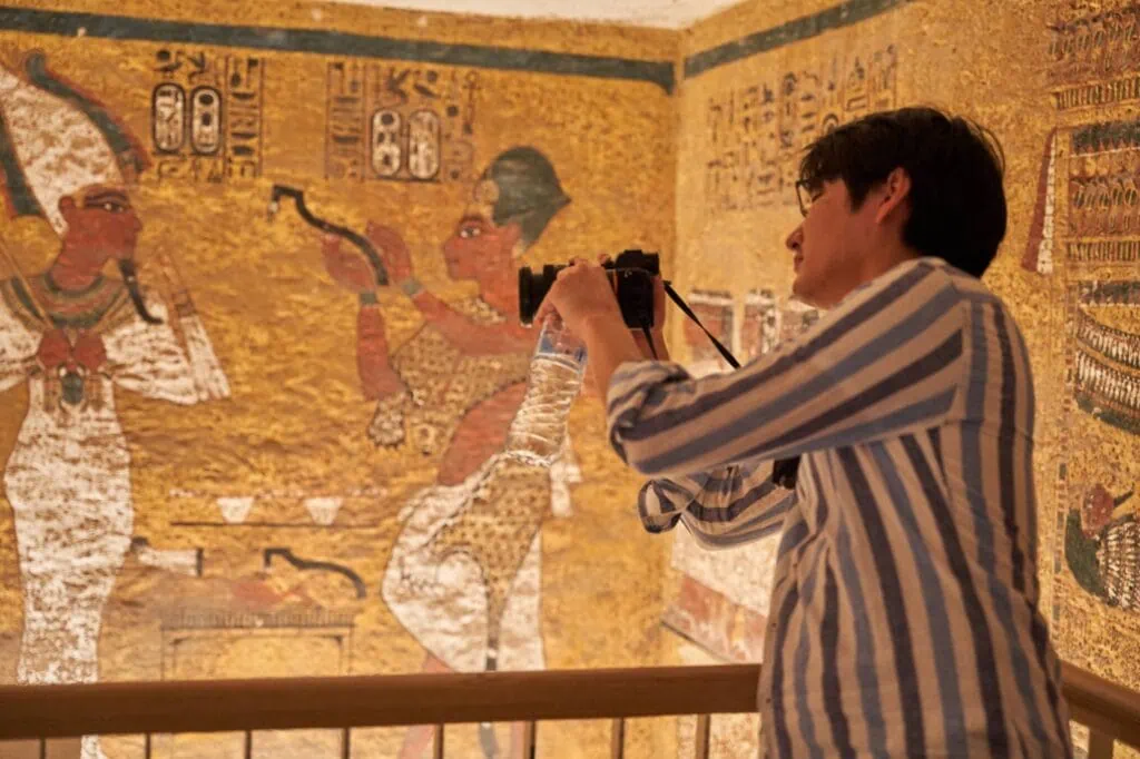 Tomb of Pharaoh Tutankhamun showing interior wall decorations with a tourist taking a photo in the Valley of the Kings, Luxor