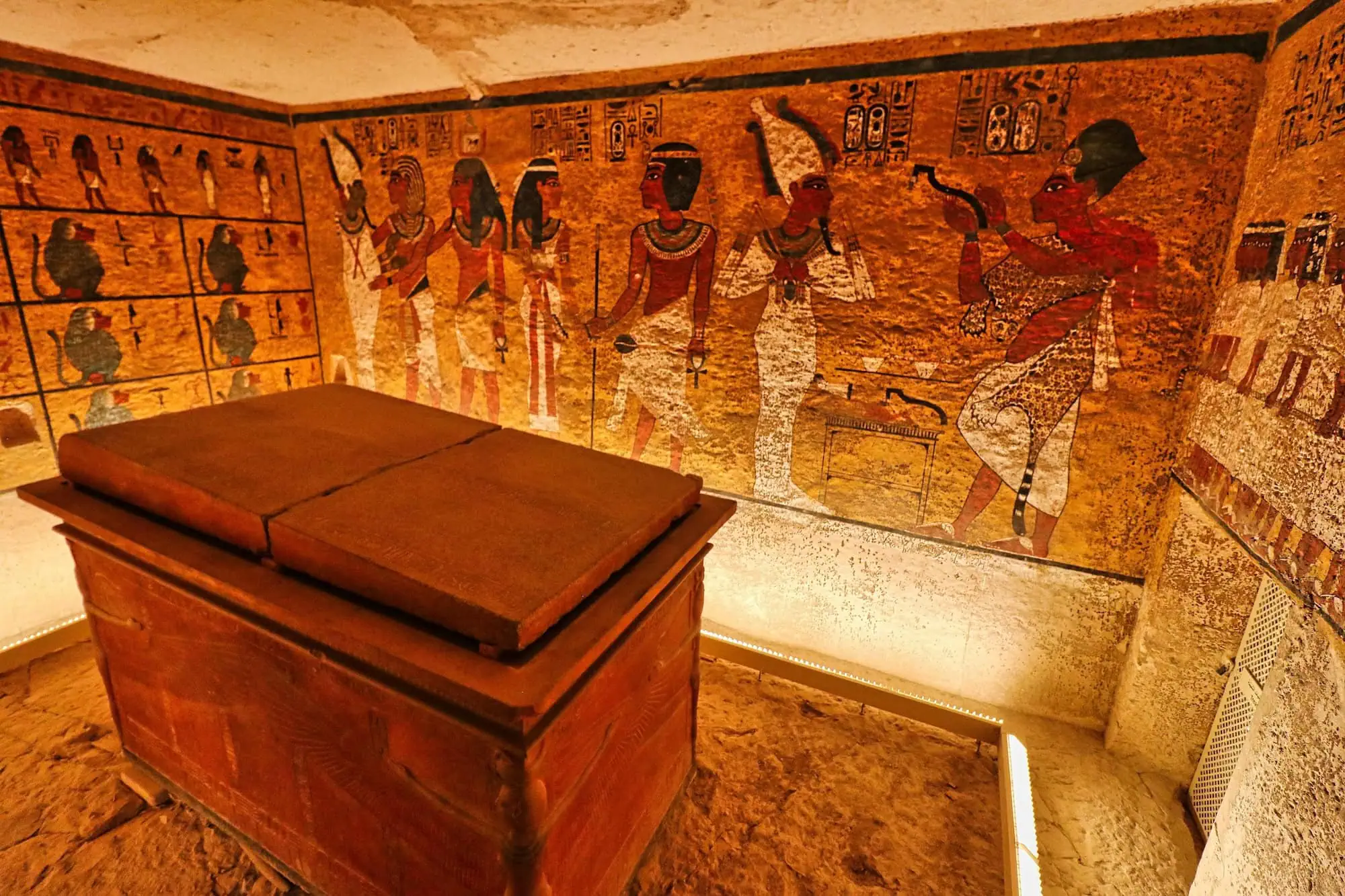 The interior of Tomb KV62 of Pharaoh Tutankhamun in the Valley of the Kings, showing the painted wall scenes and the protective glass case over the king's sarcophagus