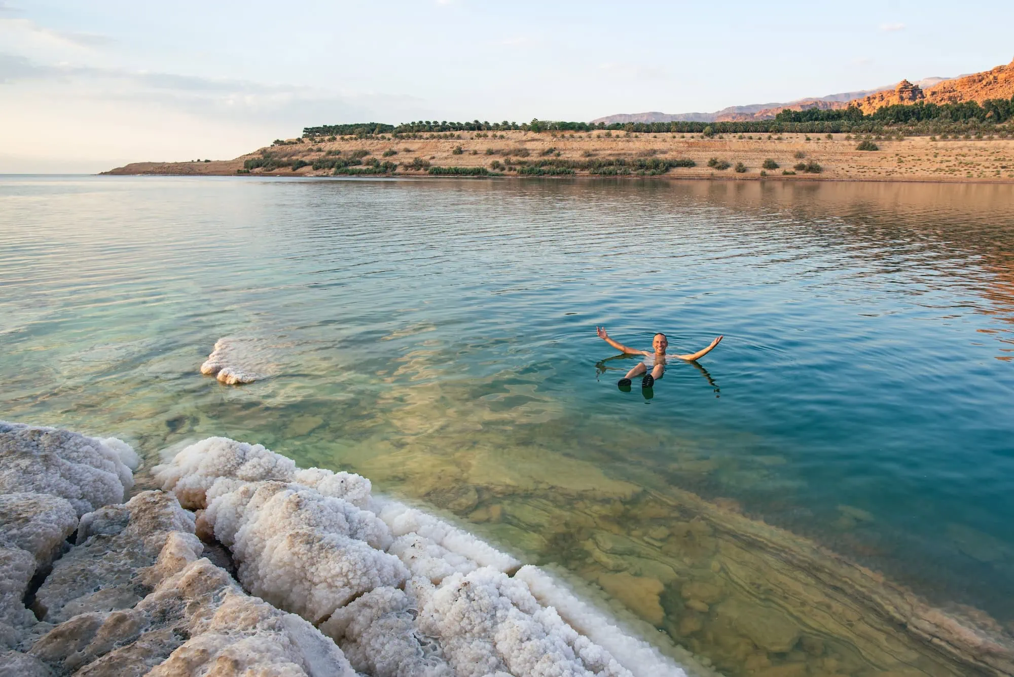 Person floating in the Dead Sea with salt formations and desert landscape