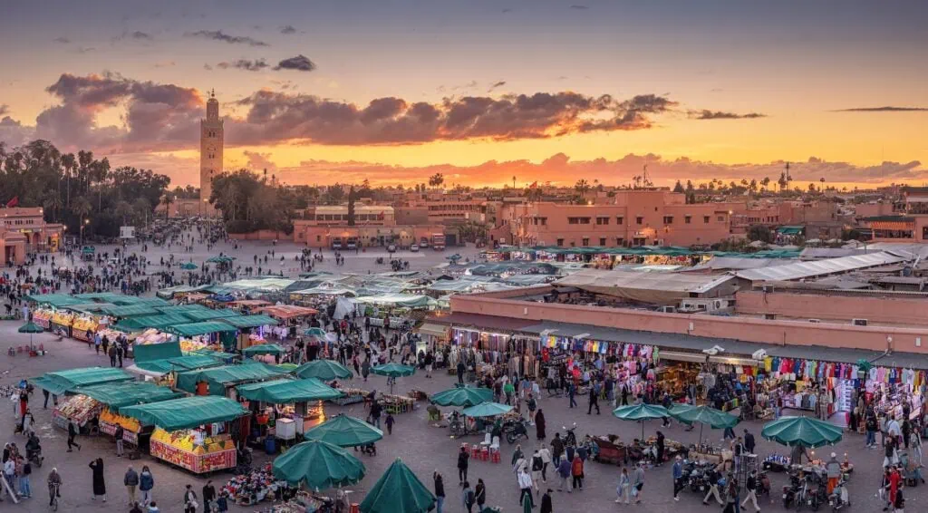 The crowded Djemaa el-Fna square in Marrakech at sunset, with the minaret of the Koutoubia Mosque rising in the background, Morocco.