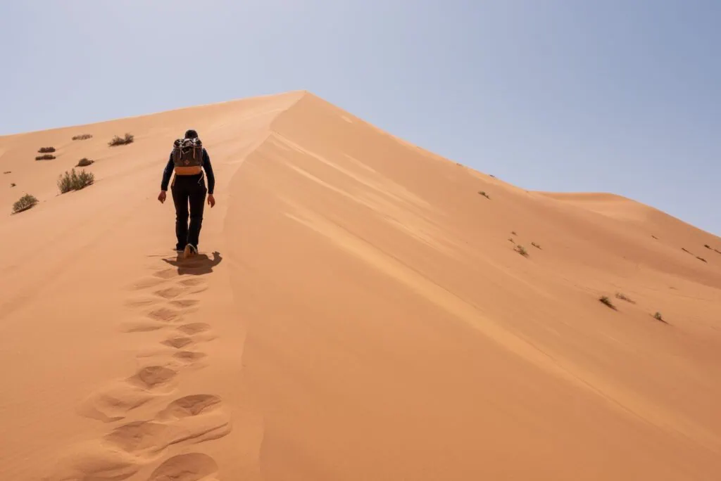 Hiker climbing the Great Dune of Merzouga in Erg Chebbi, the largest dune field in Morocco's Sahara, reaching heights of around 150 metres.