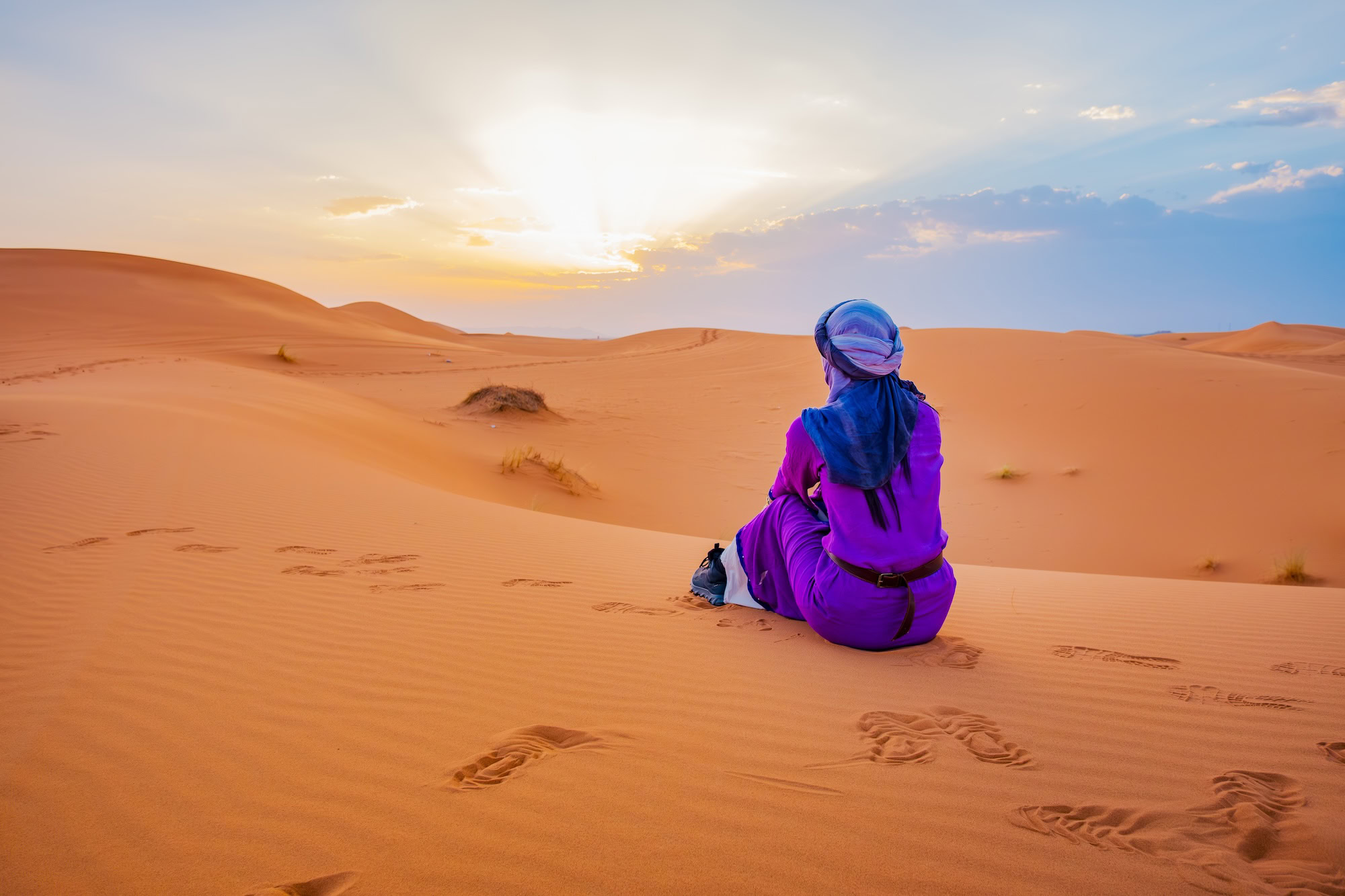 Person in traditional robes enjoying the Sahara Desert at sunrise