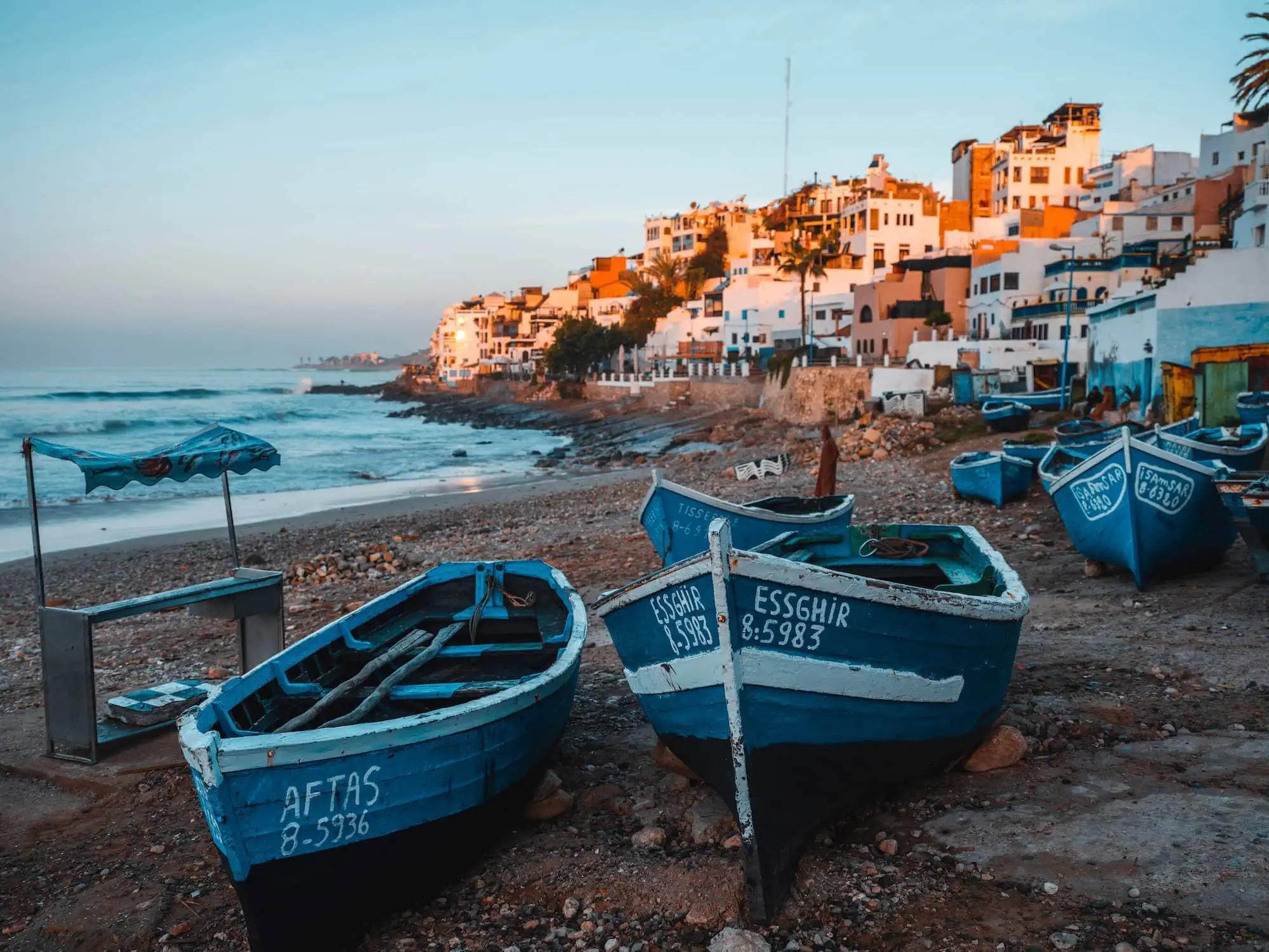 Morning view of Taghazout fishing village with blue boats and coastal cliffs