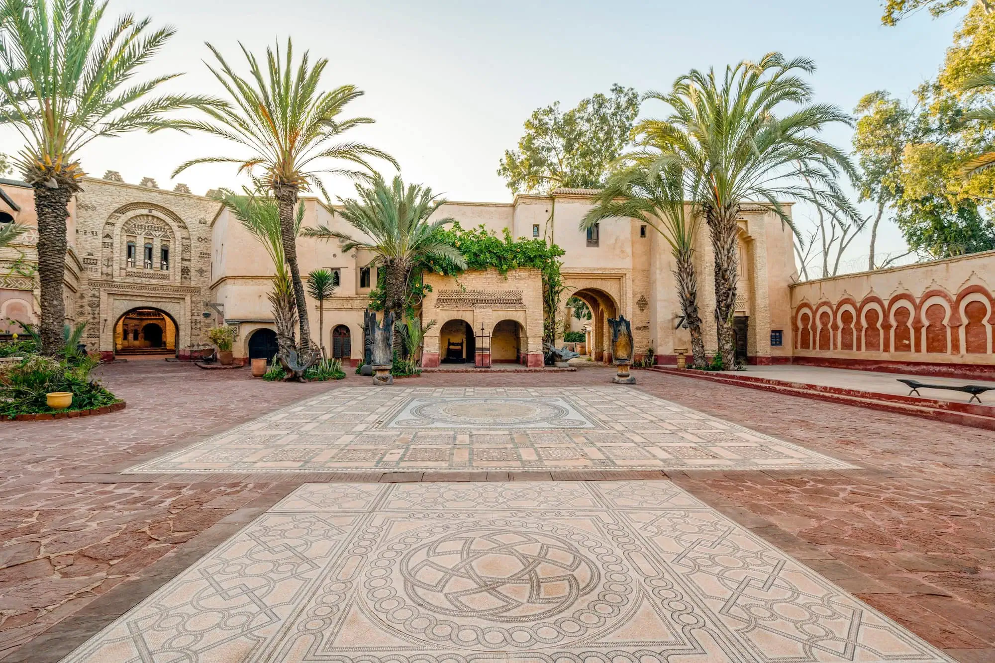 Traditional Moroccan medina courtyard with arched walkways, palm trees and geometric mosaic flooring