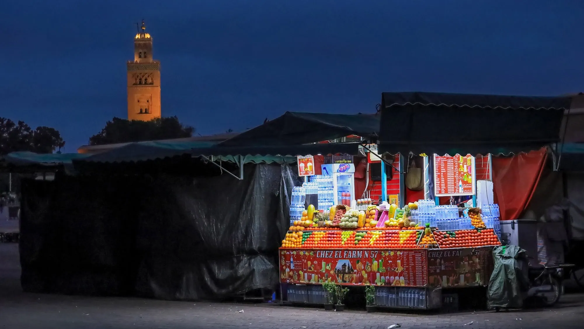 Traditional Moroccan mosque with illuminated minaret near market stalls at Jemaa el-Fna square