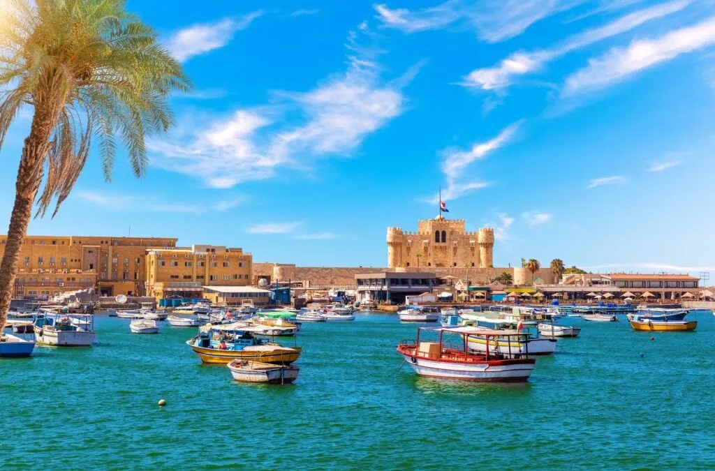 Traditional boats anchored in Alexandria harbour with the stone Citadel of Qaitbay on the Mediterranean waterfront behind, Egypt.