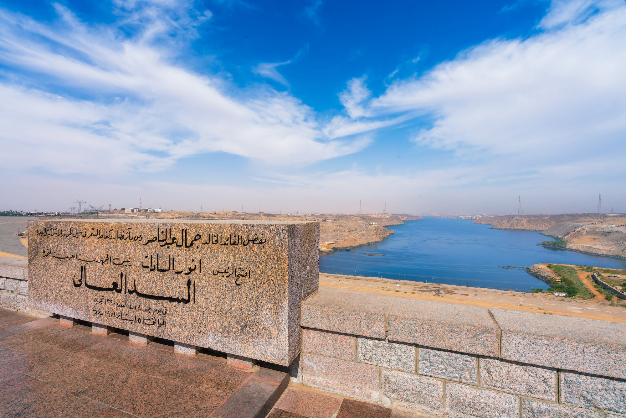 Stone monument with Arabic inscription overlooking Aswan High Dam reservoir and desert landscape